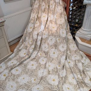 Large beige fabric with oversized white flowers laid as a floor-length draped display, showing floral upholstery or drapery material.