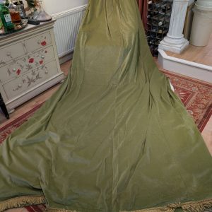 Large olive-green fabric draped over a tall object in a vintage-style room, with a painted dresser, sunflower artwork, and wine rack nearby.