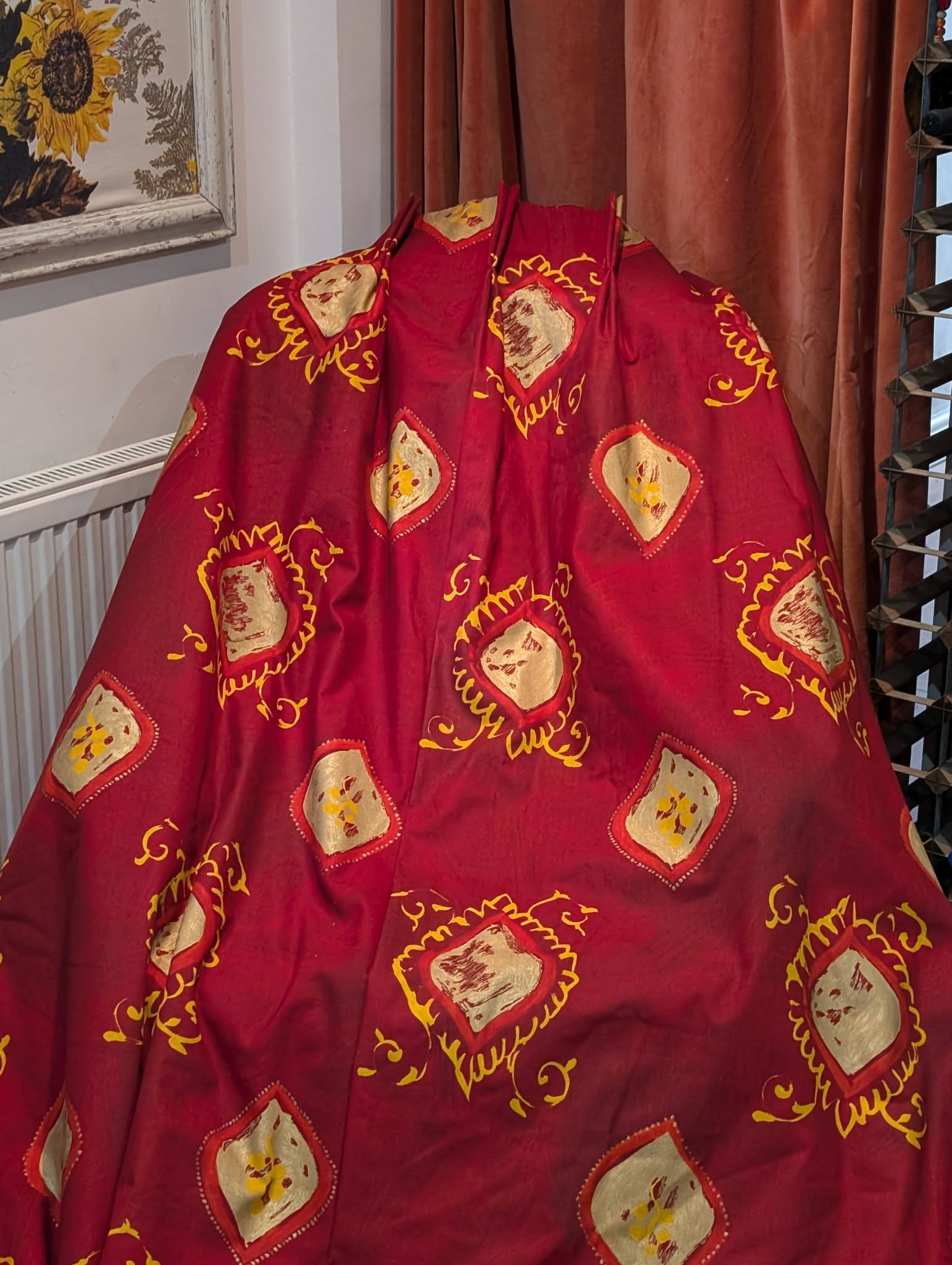 lauren3 - Divinely Vintage Interiors Red fabric with cream diamond motifs and yellow trim draped indoors beside a sunflower painting and brown curtains.