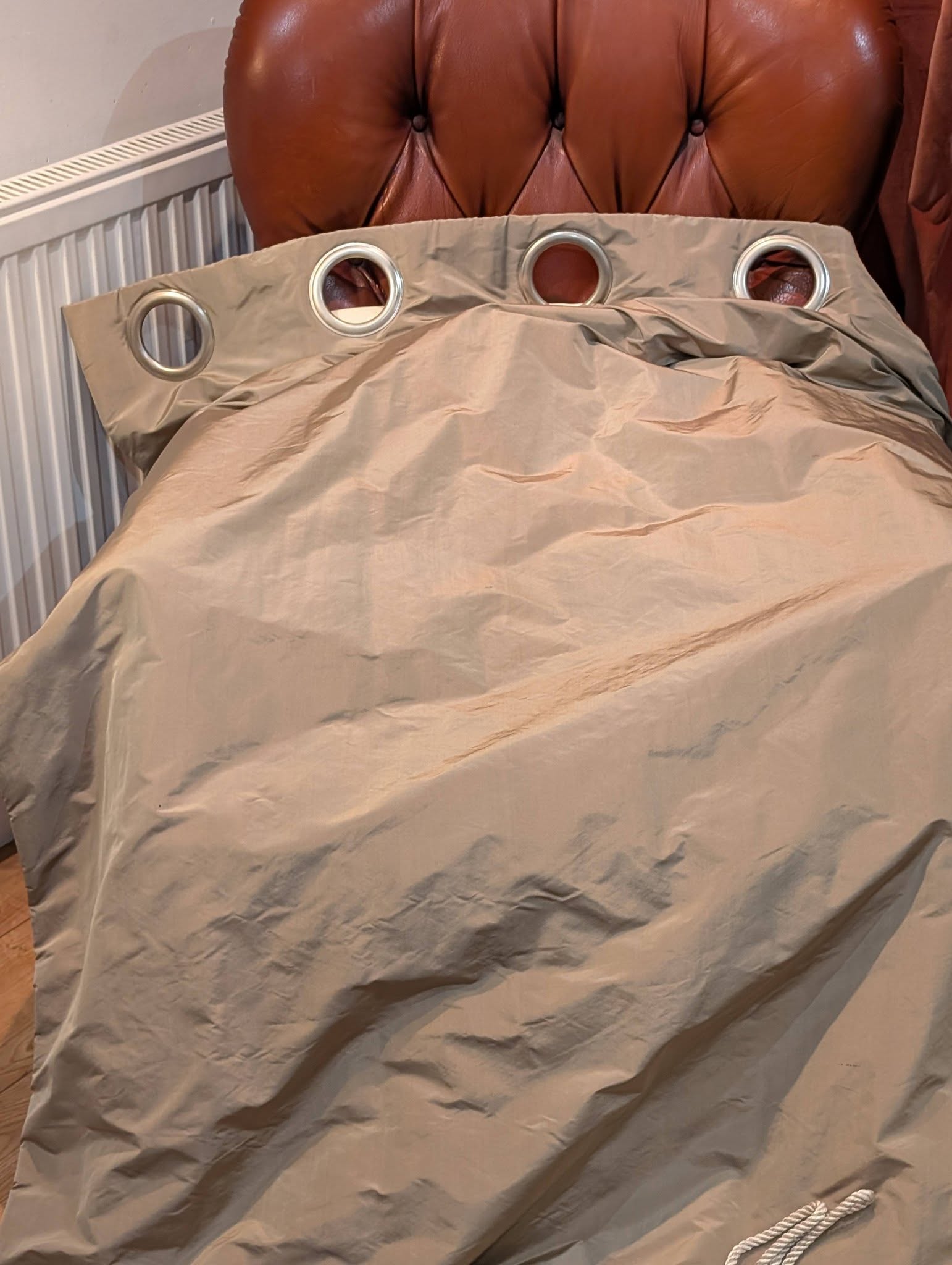 rach23 - Divinely Vintage Interiors Beige fabric panel with four metal grommets laid over a surface beside a tufted brown headboard.