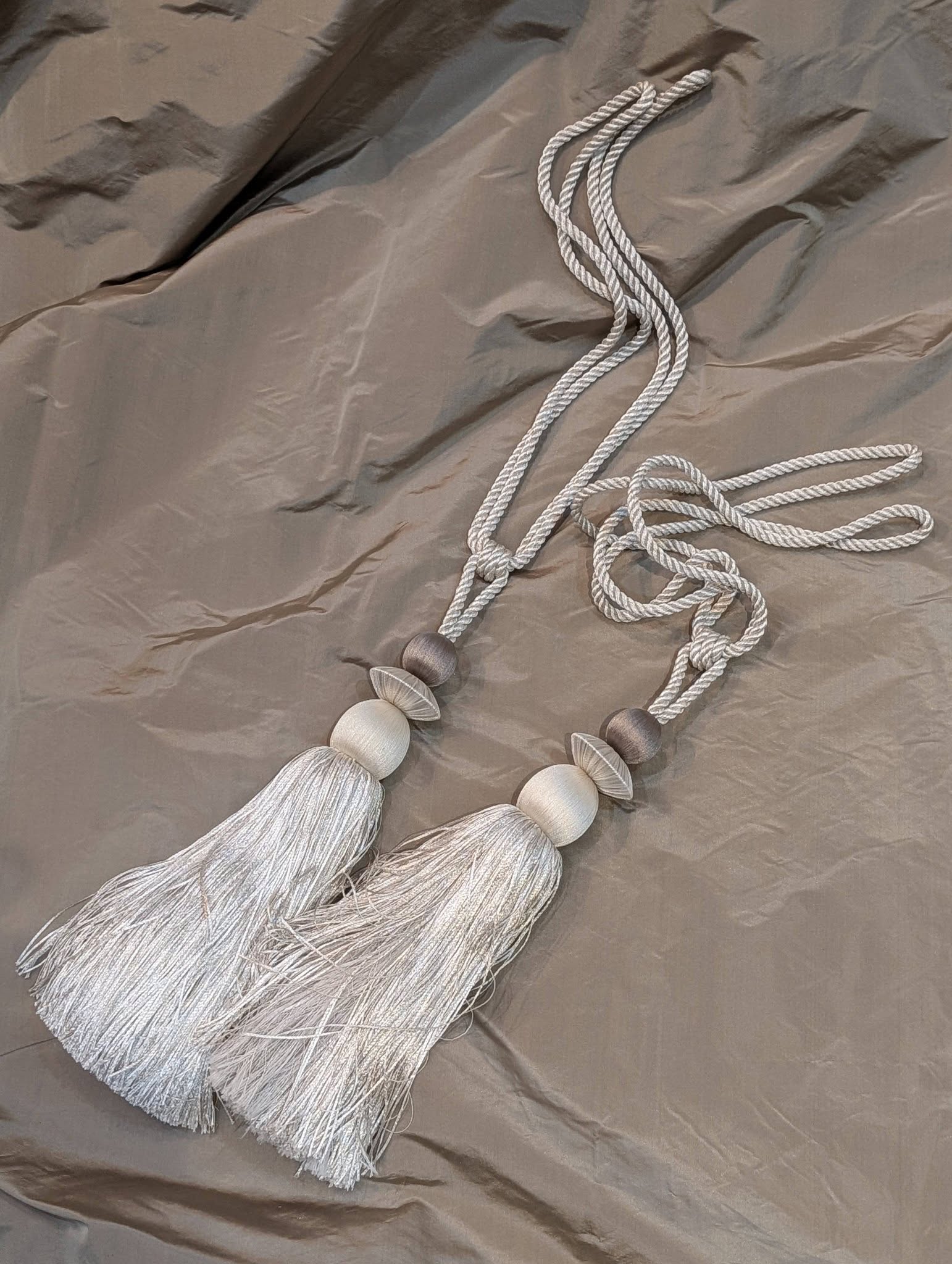 rach24 - Divinely Vintage Interiors Decorative gray tassel garland with round beads laid on a metallic fabric background