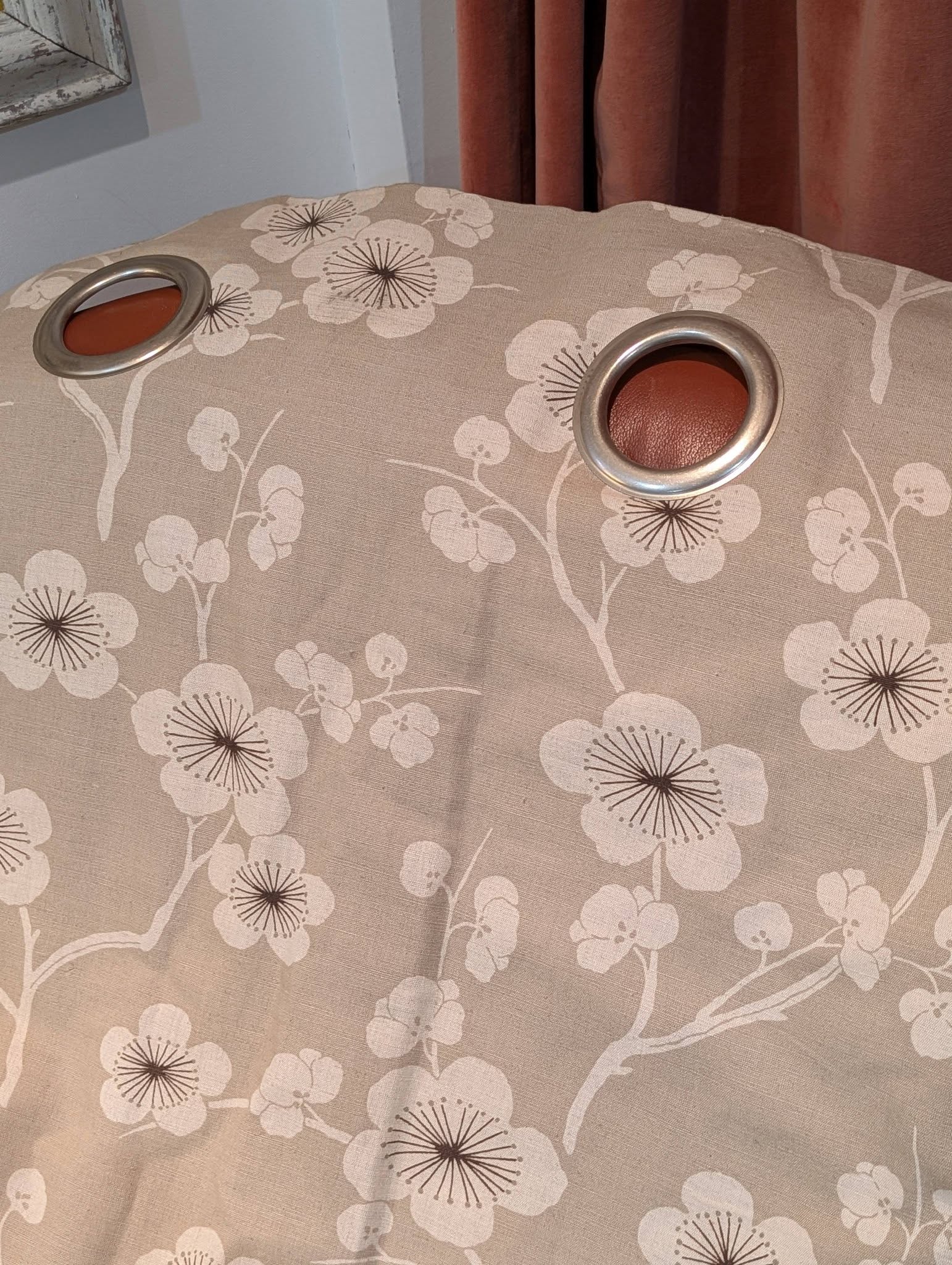 rach34 - Divinely Vintage Interiors Close-up of a beige floral-patterned fabric with two silver metal grommets showing red inserts.