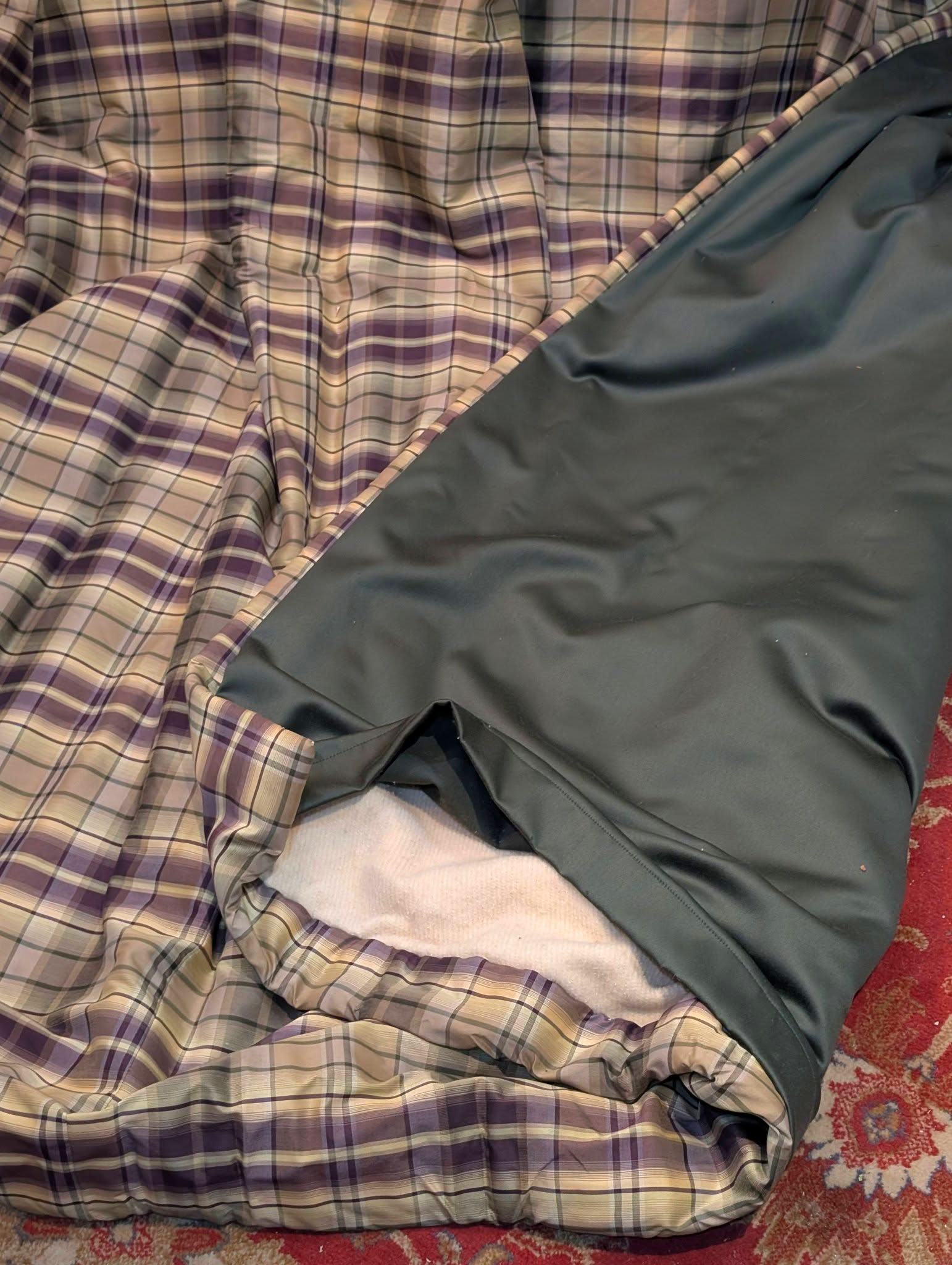 rach4 - Divinely Vintage Interiors Crumpled plaid blanket in purple, beige, and white beside a dark green fabric on a red carpeted floor