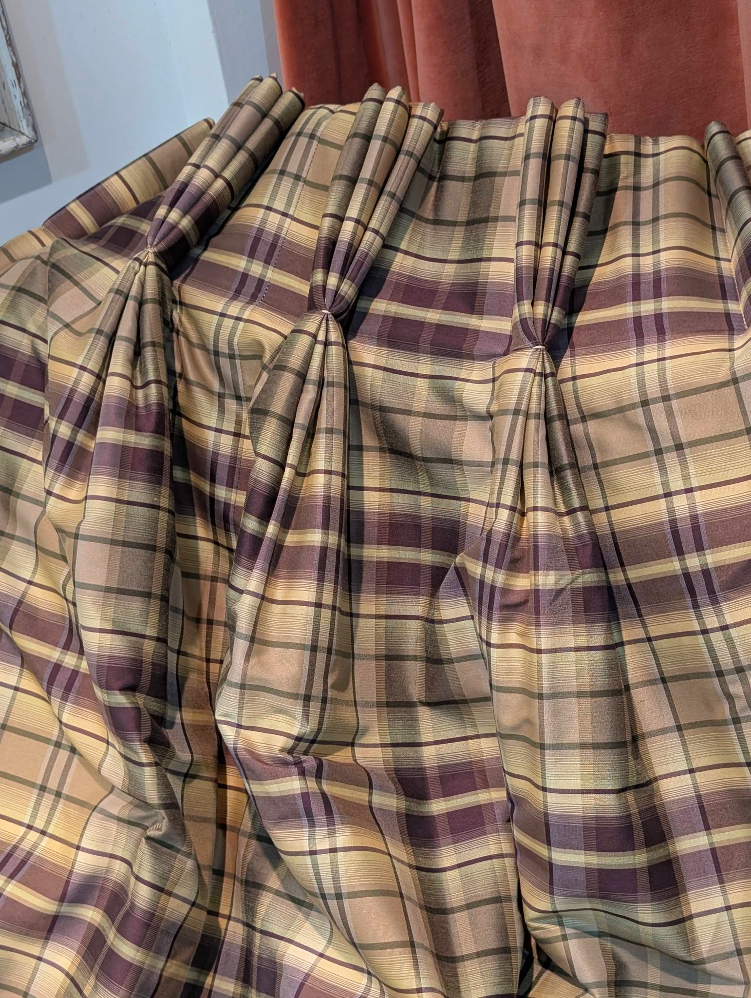 rach5 - Divinely Vintage Interiors Rows of plaid fabric curtains in beige, olive, and burgundy draped in soft folds.