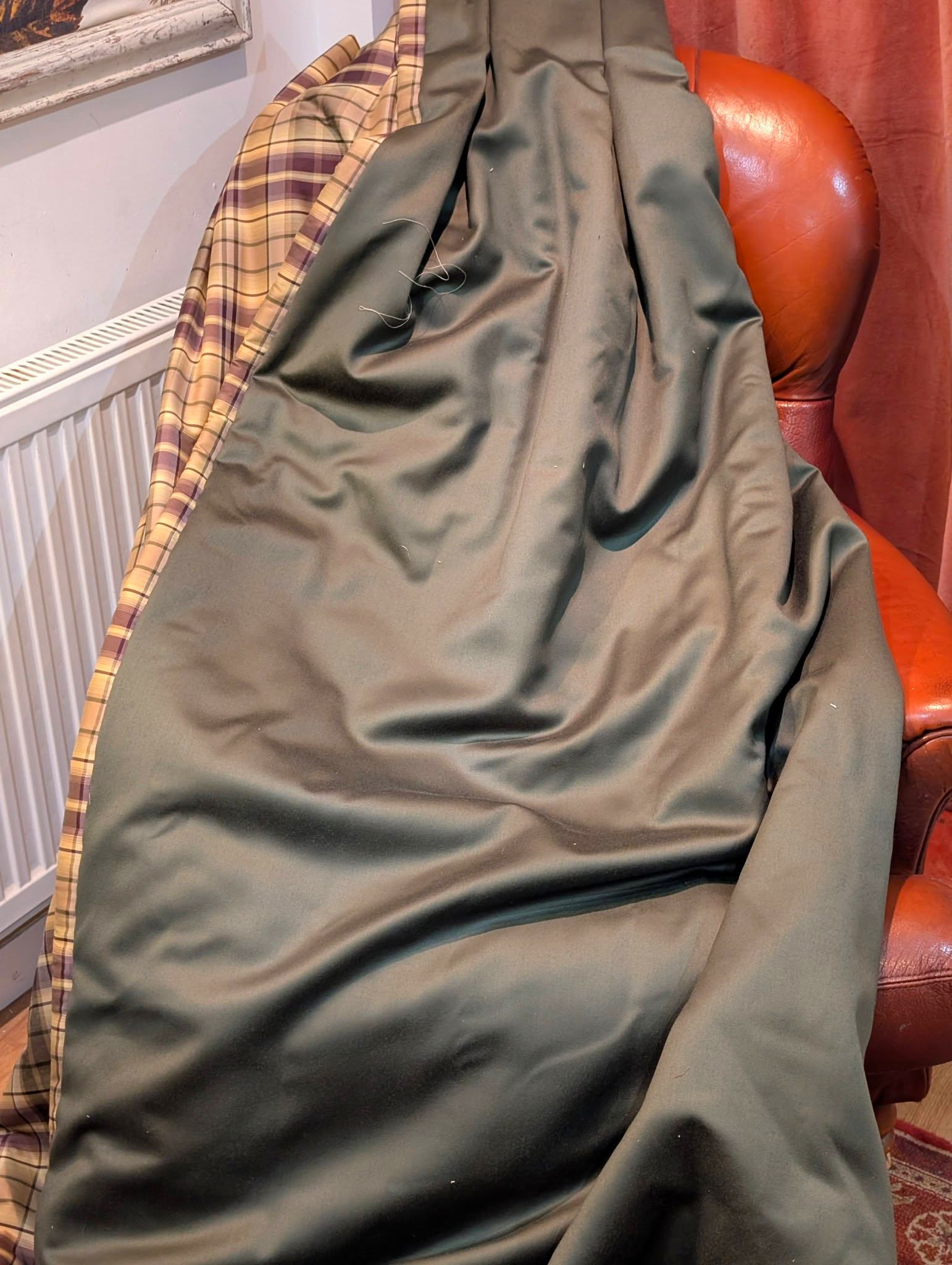 rach6 - Divinely Vintage Interiors Olive-green coat draped over a brown leather chair with plaid lining visible nearby beside a radiator.