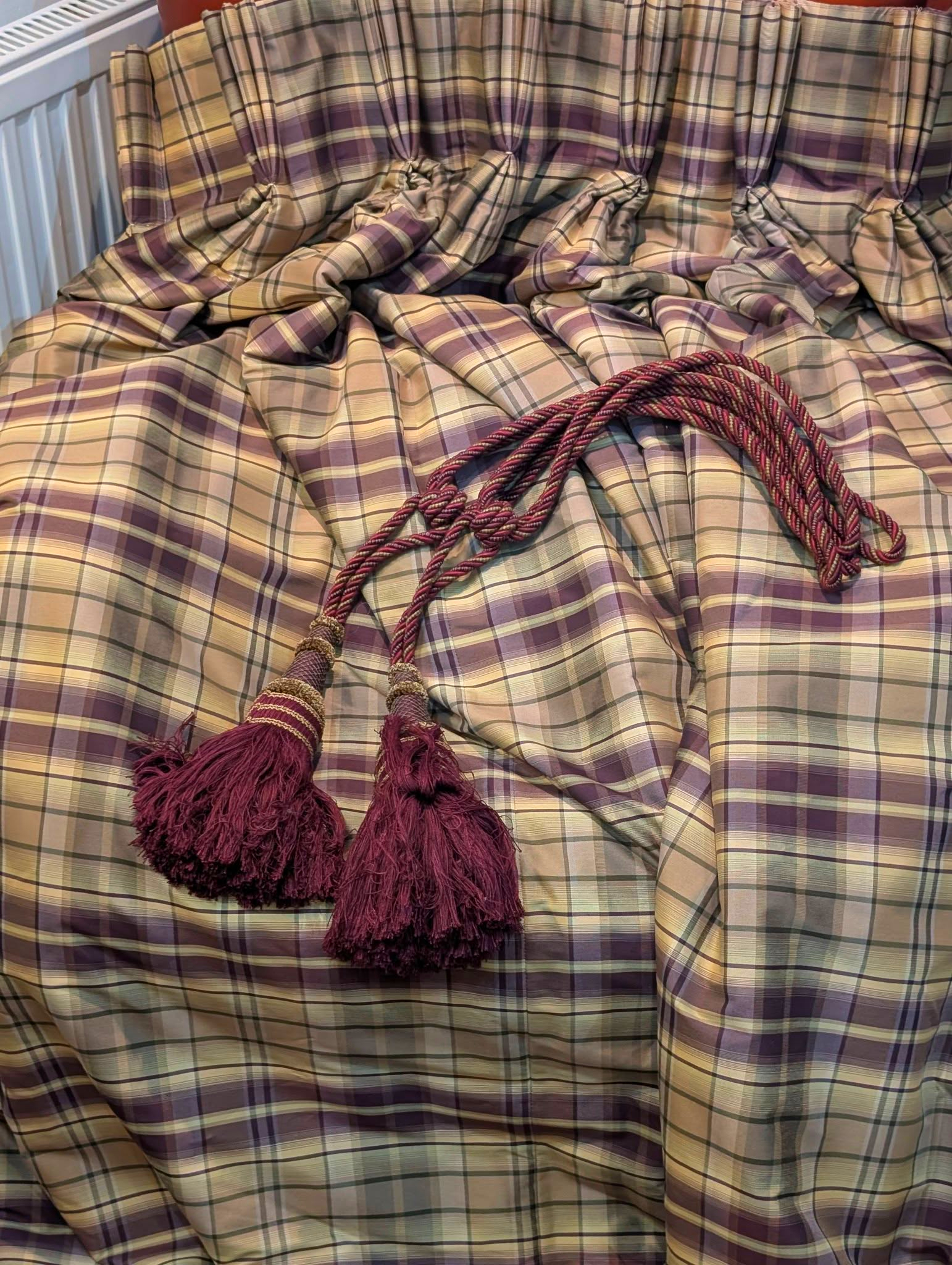 rach7 - Divinely Vintage Interiors Close-up view of a plaid bedspread in beige, purple, and cream tones with maroon tassels lying across it.
