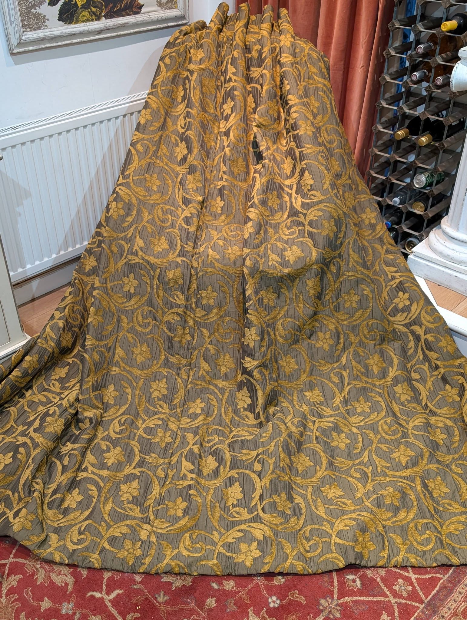 rachel1 - Divinely Vintage Interiors Gold floral-patterned fabric draped over a stand, covering a rounded display area near a wine rack in a room with a red patterned rug.