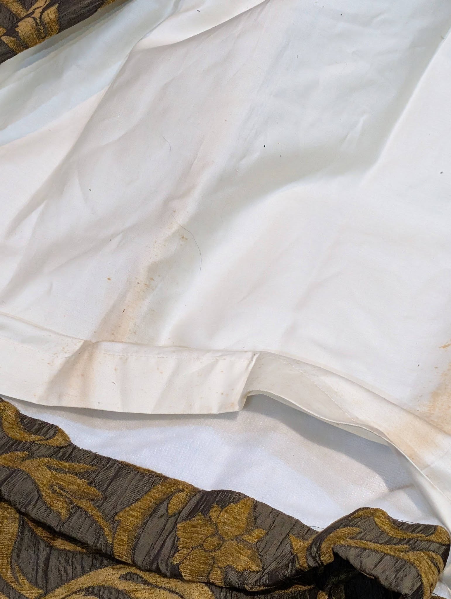 rachel5 - Divinely Vintage Interiors Close-up of white wrinkled fabric or napkin on a dark gold and black patterned trim.