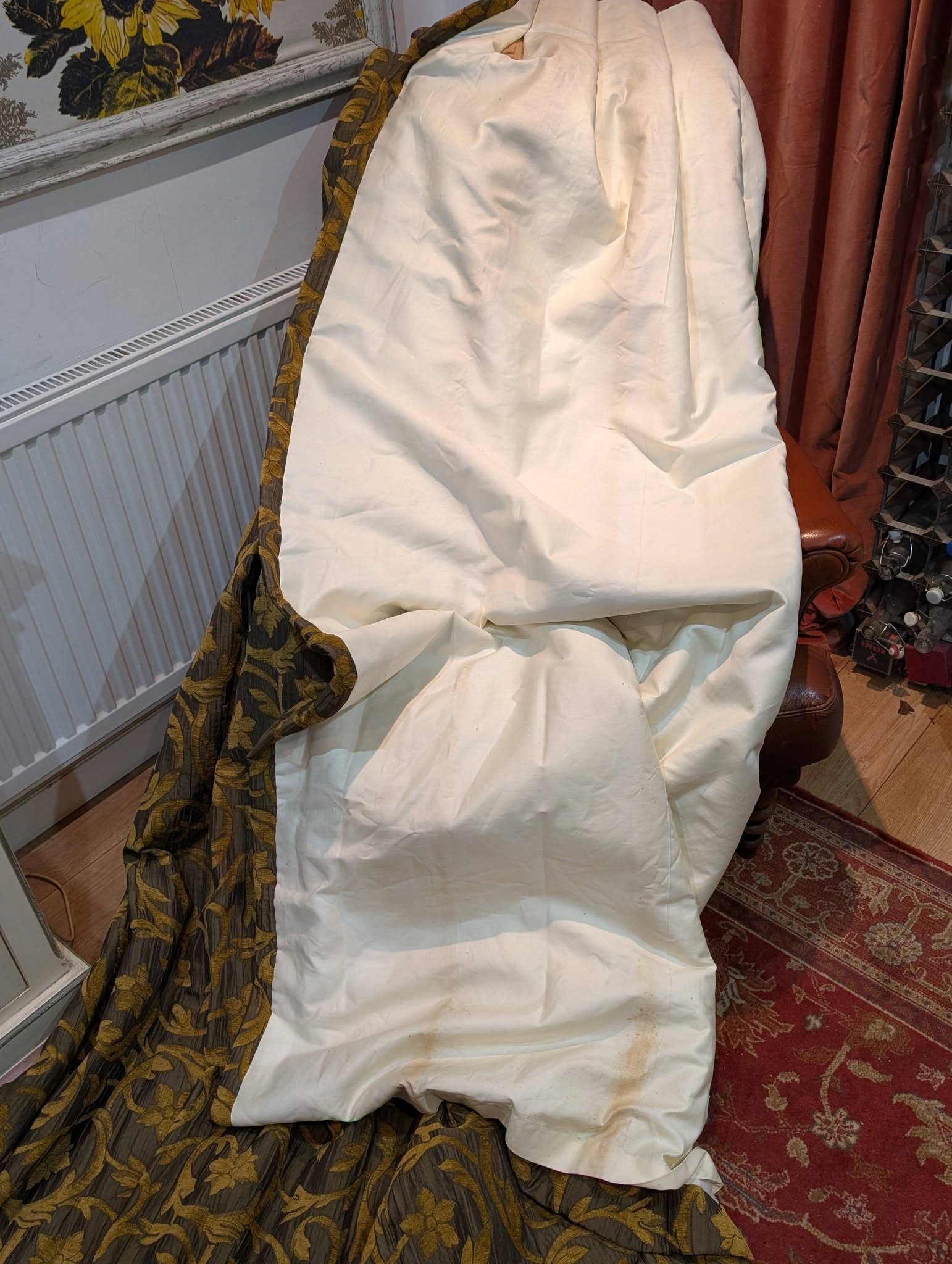 rachel7 - Divinely Vintage Interiors White fabric draped over a chair/sofa in a room, with a gold-and-brown patterned curtain beside it and a radiator along the wall behind.