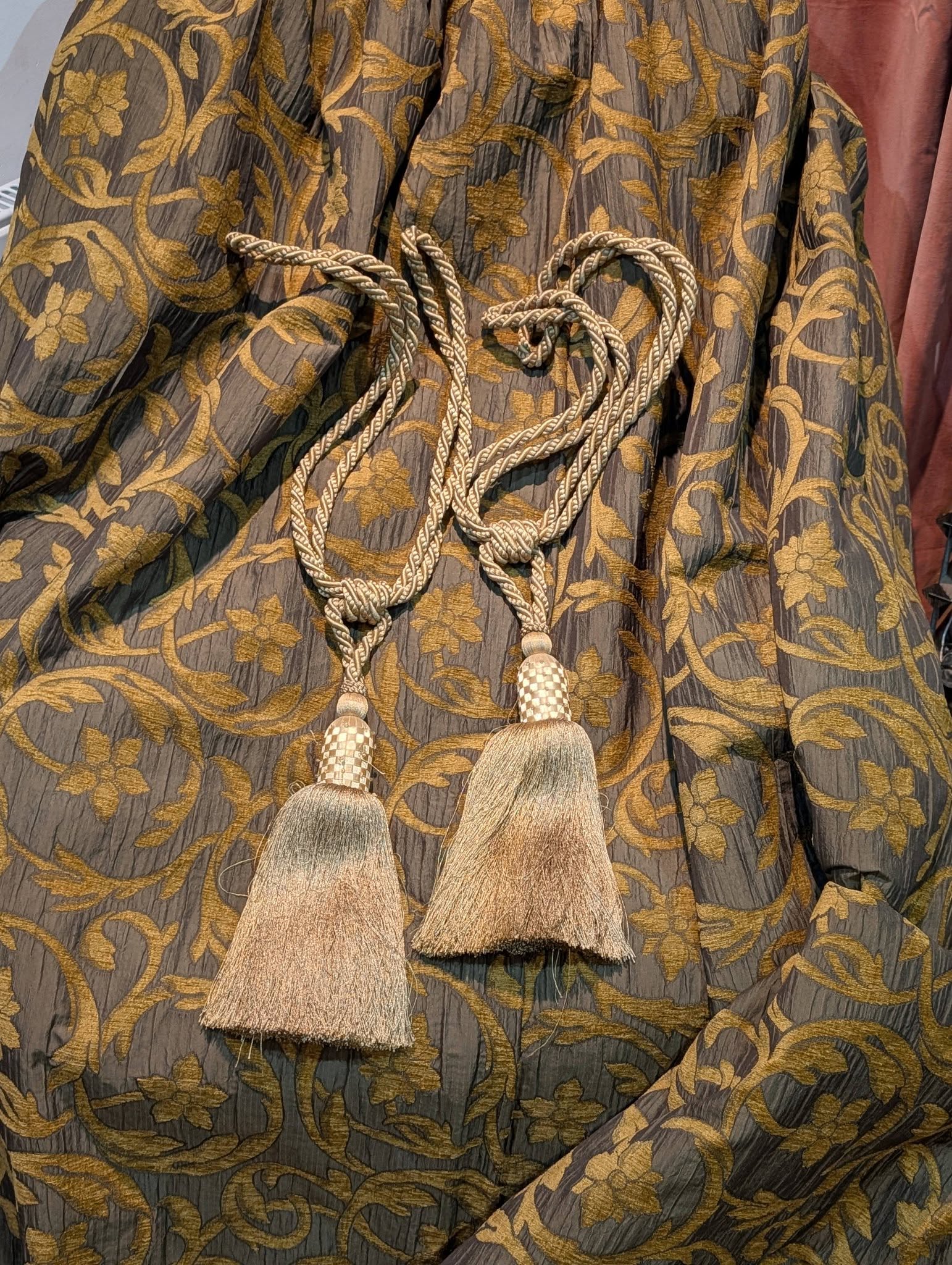 rachel8 - Divinely Vintage Interiors Close-up of a gray fabric with intricate gold floral embroidery and a braided rope belt with tassels tied at the waist.