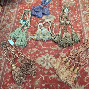Decorative tassels and braided cords arranged on a red oriental rug.