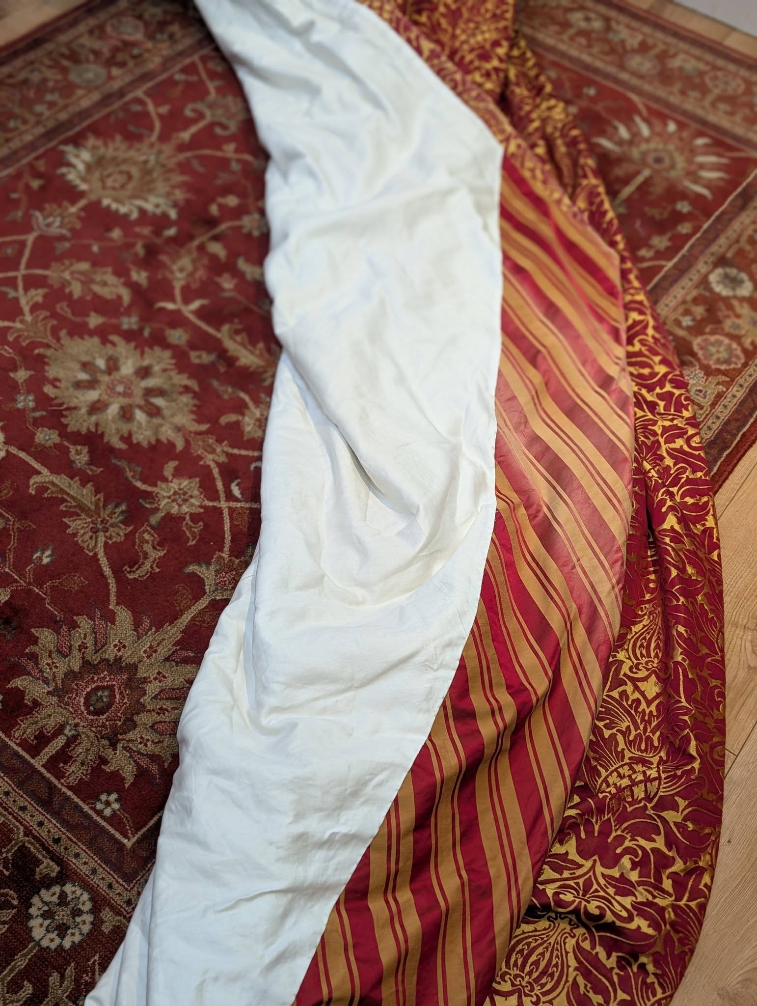 rich15 - Divinely Vintage Interiors White fabric laid out on a red and gold patterned rug.