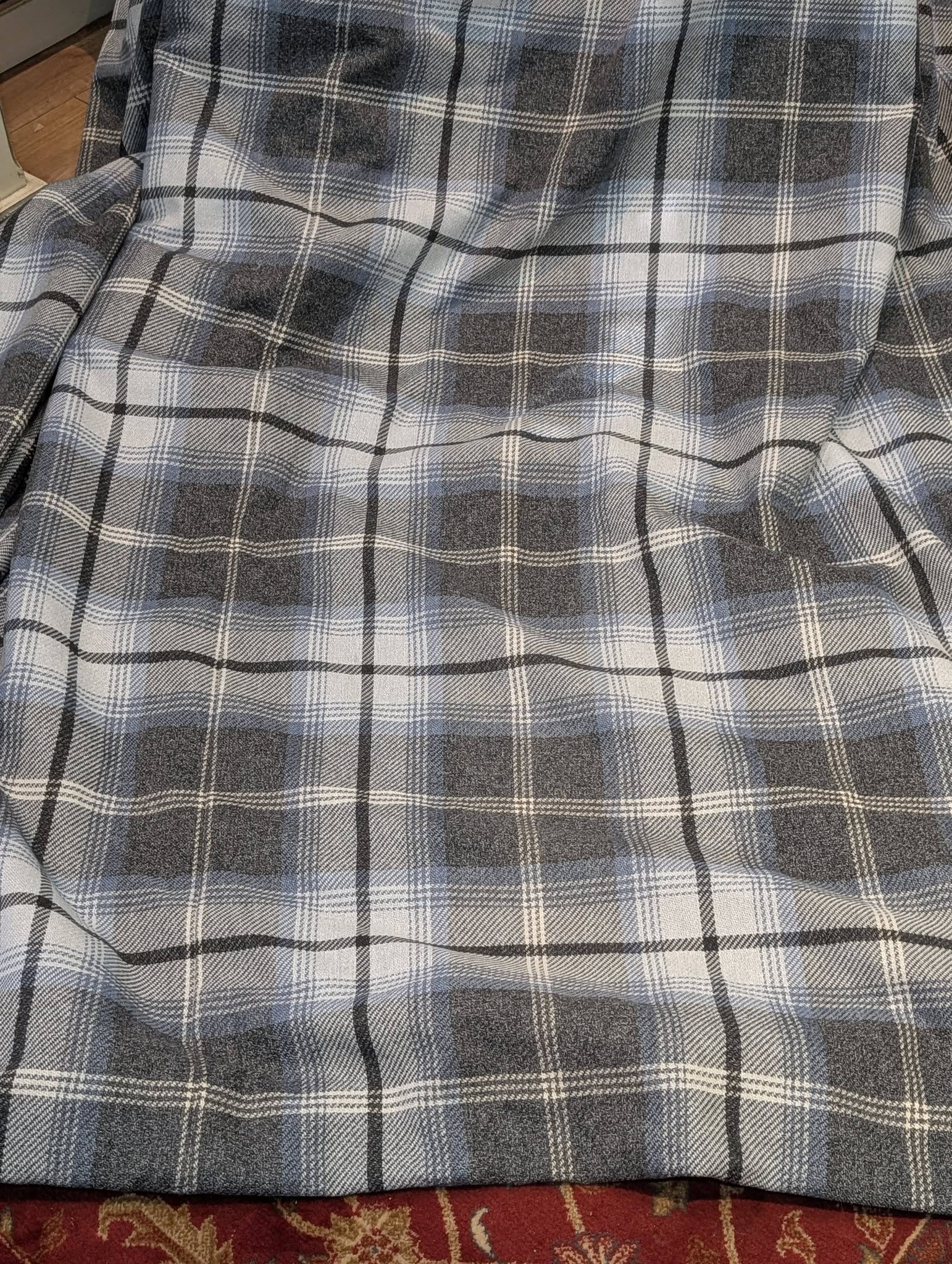 richard2 - Divinely Vintage Interiors Gray and blue plaid blanket draped over a chair, with a red patterned rug visible at the bottom edge.
