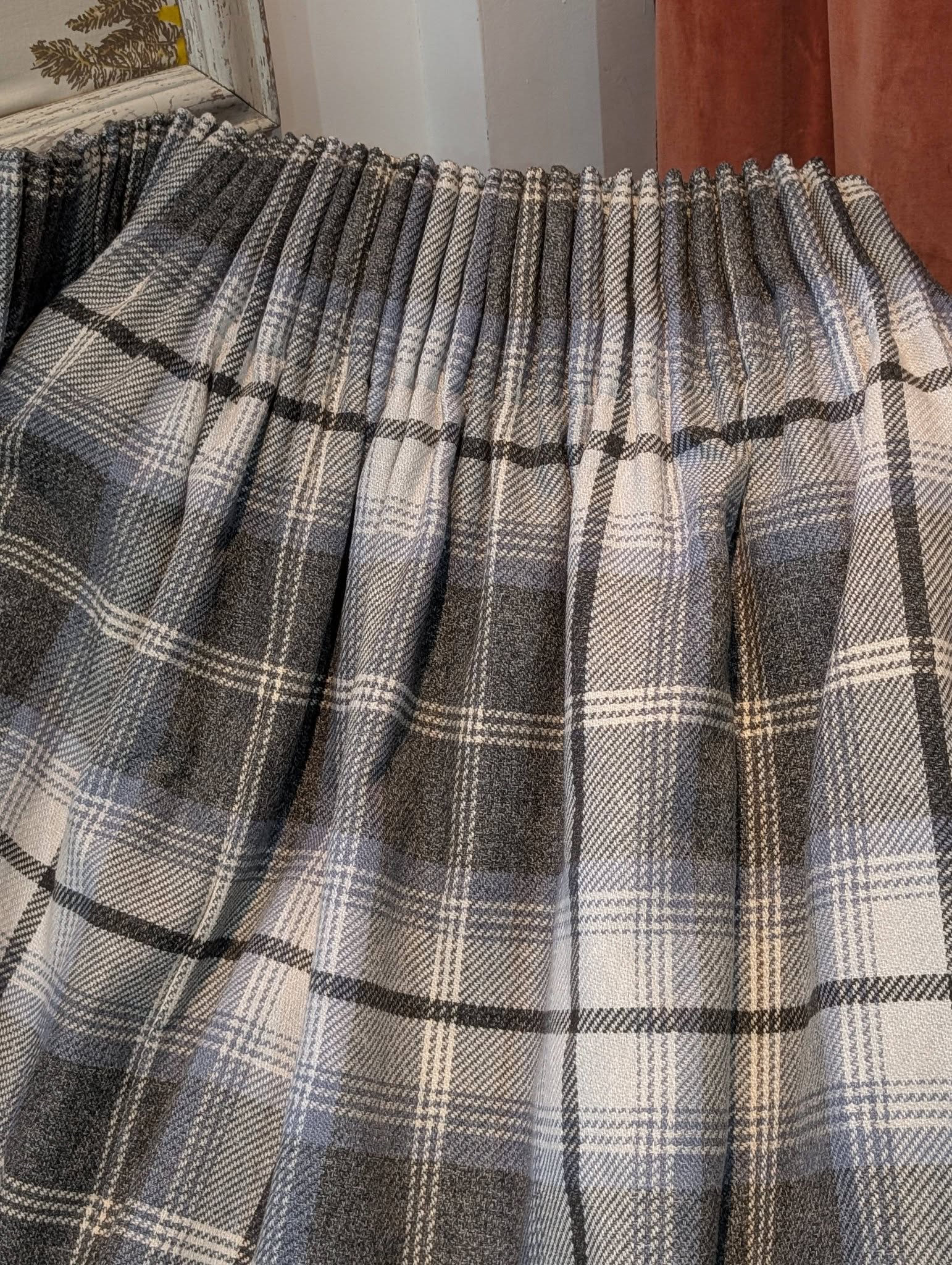 richard5 - Divinely Vintage Interiors Close-up of a gray plaid blanket or fabric with white and dark stripes folded in ripples along a window sill area.