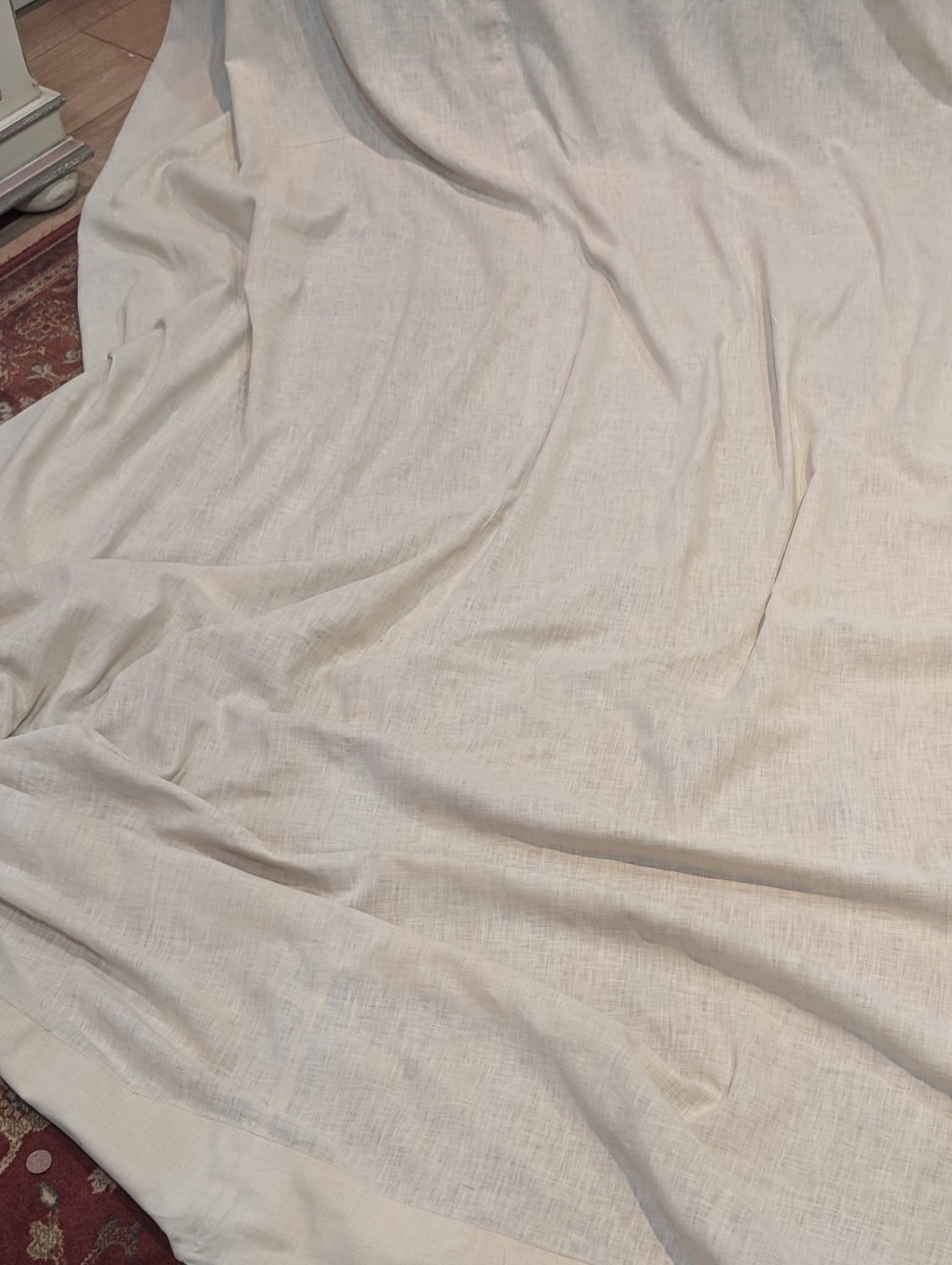 drew5 - Divinely Vintage Interiors Cream linen sheet draped over a surface with wrinkles; a red patterned rug edge visible in the lower left.