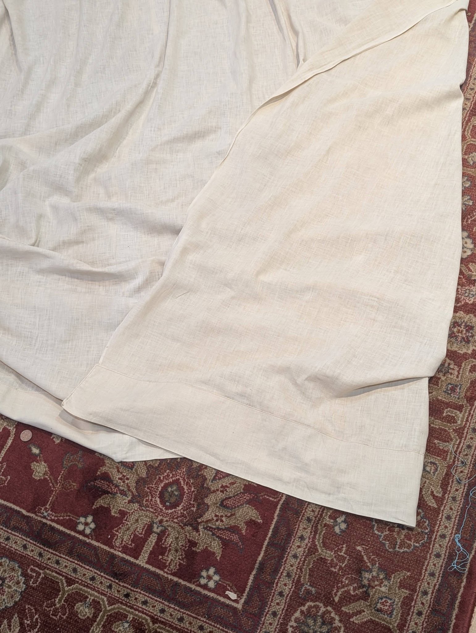 drew7 - Divinely Vintage Interiors Cream linen sheet spread over a red patterned rug on the floor, with visible folds and wrinkles.