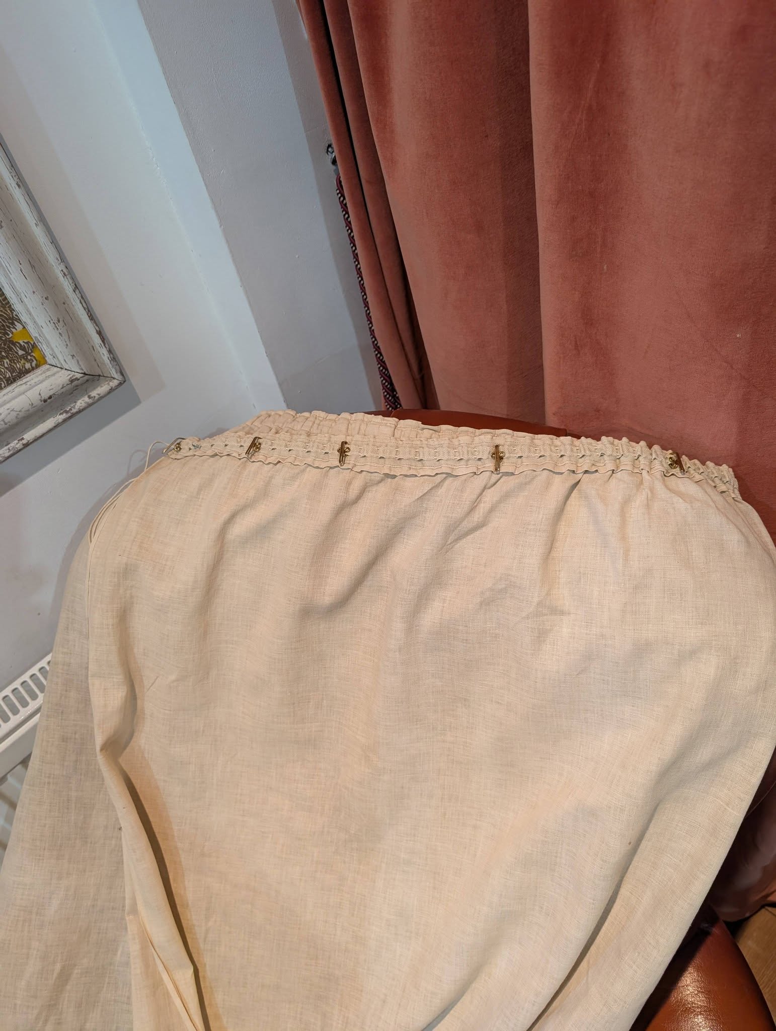 drew9 - Divinely Vintage Interiors Close-up of beige, textured fabric draped over a chair, with a pale blue wall and pink curtains in the background.