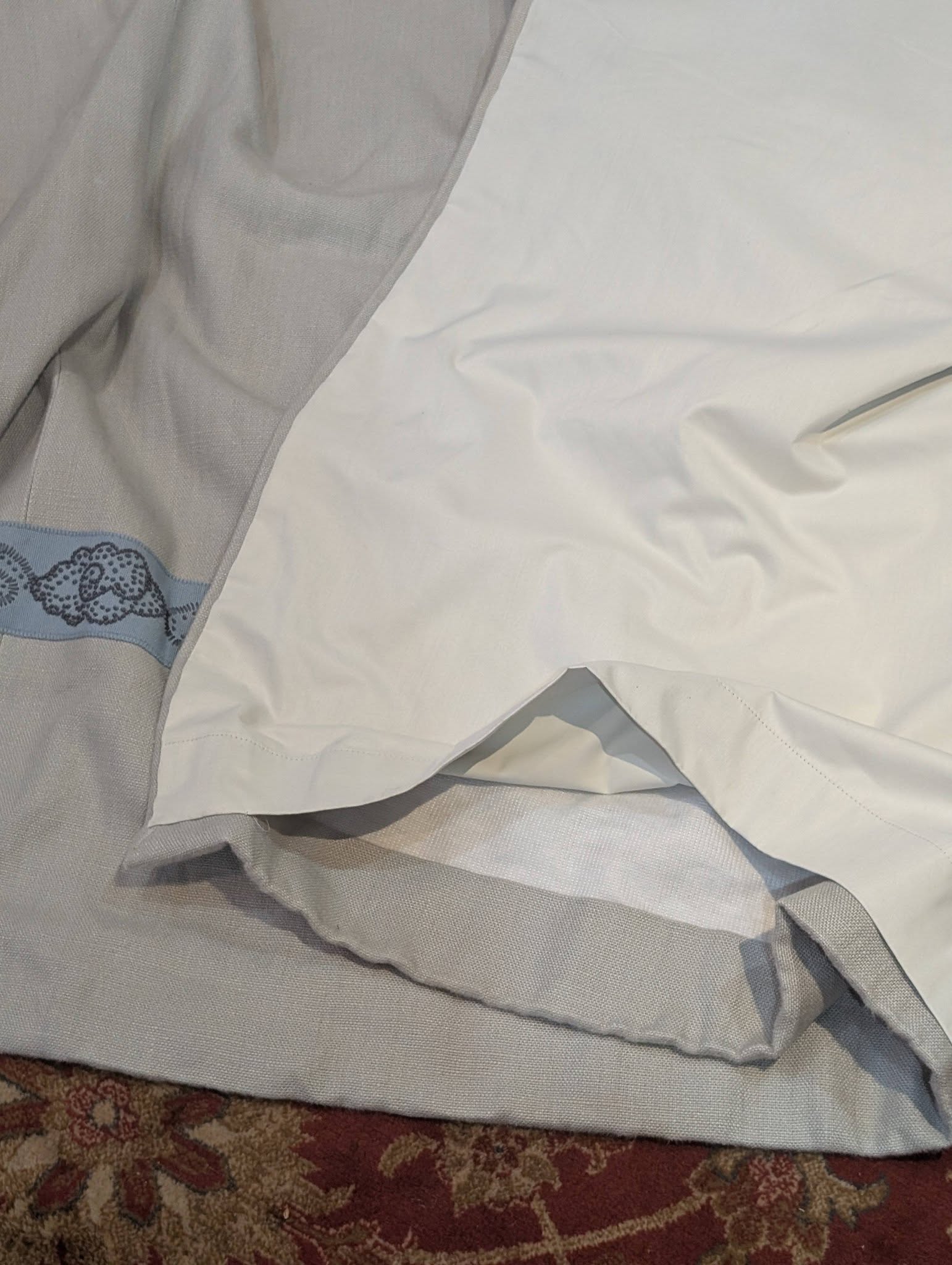 hannah14 - Divinely Vintage Interiors Crinkled white bedsheets and a gray fabric with blue lace trim, lying on a patterned rug.