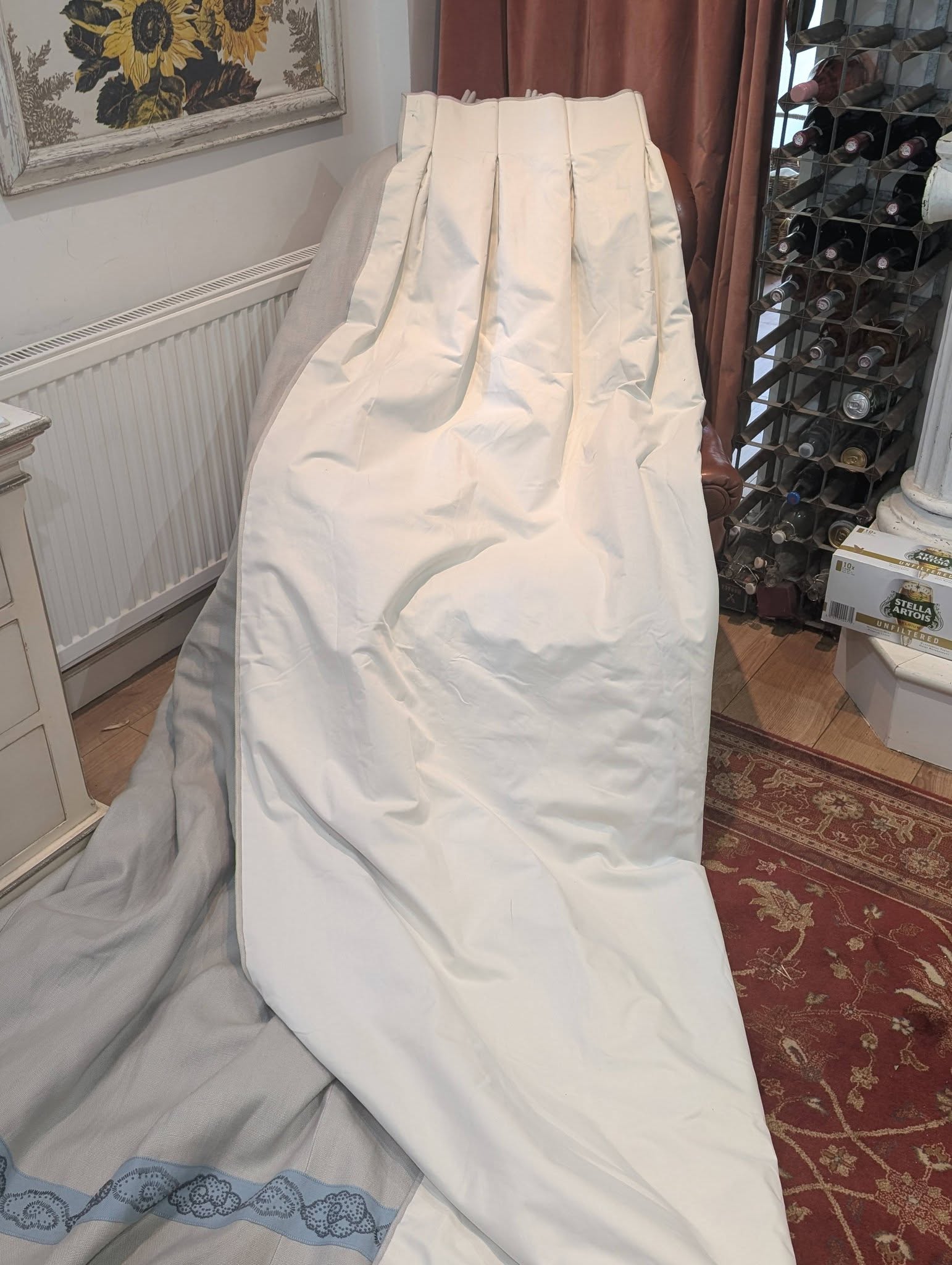 hannah16 - Divinely Vintage Interiors Large light-gray fabric cover draped over furniture in a cozy room; wine rack and brown curtains visible in the background.