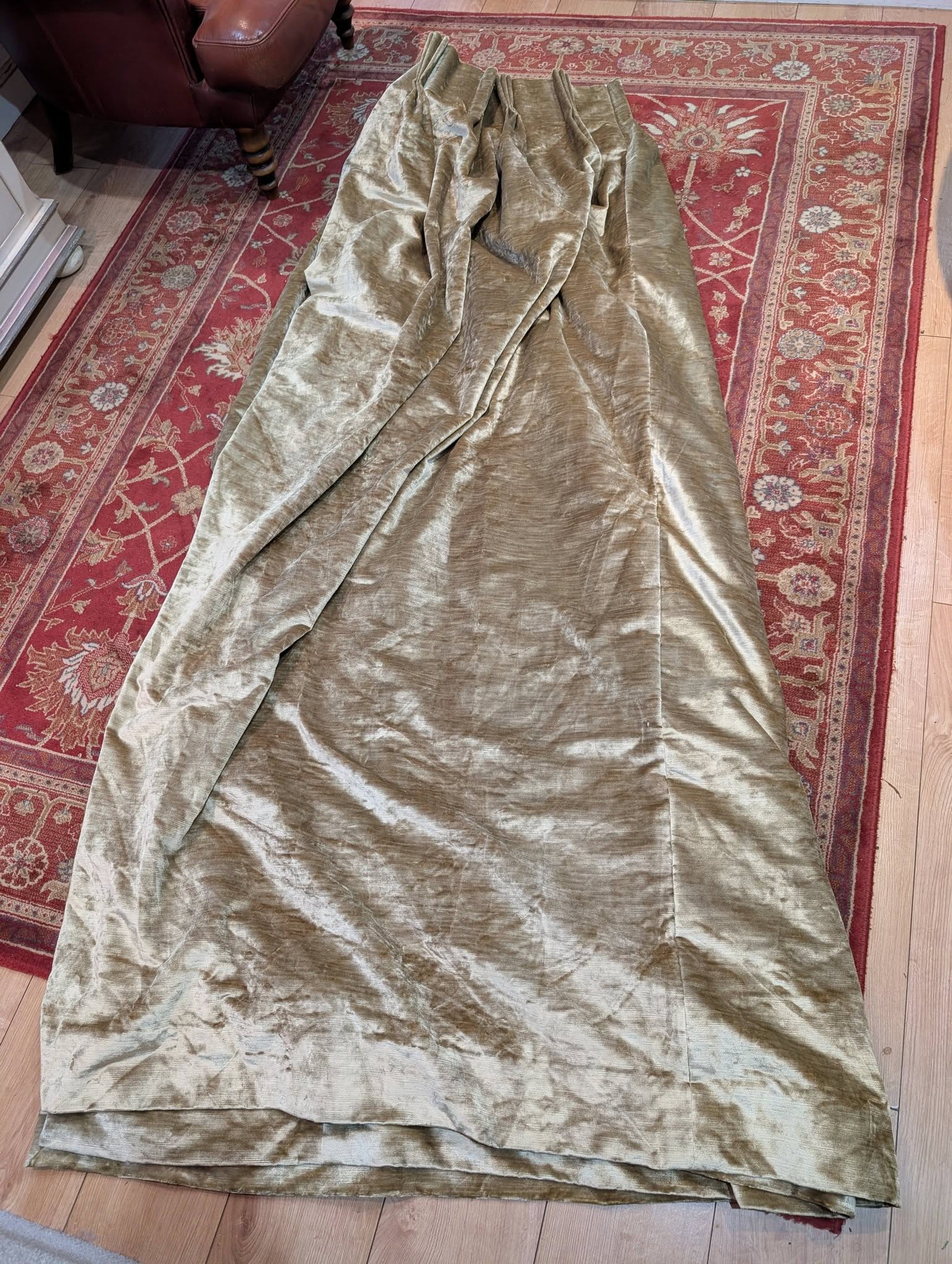 judith12 - Divinely Vintage Interiors Olive velvet fabric laid out on a red patterned rug, covering a wooden floor.