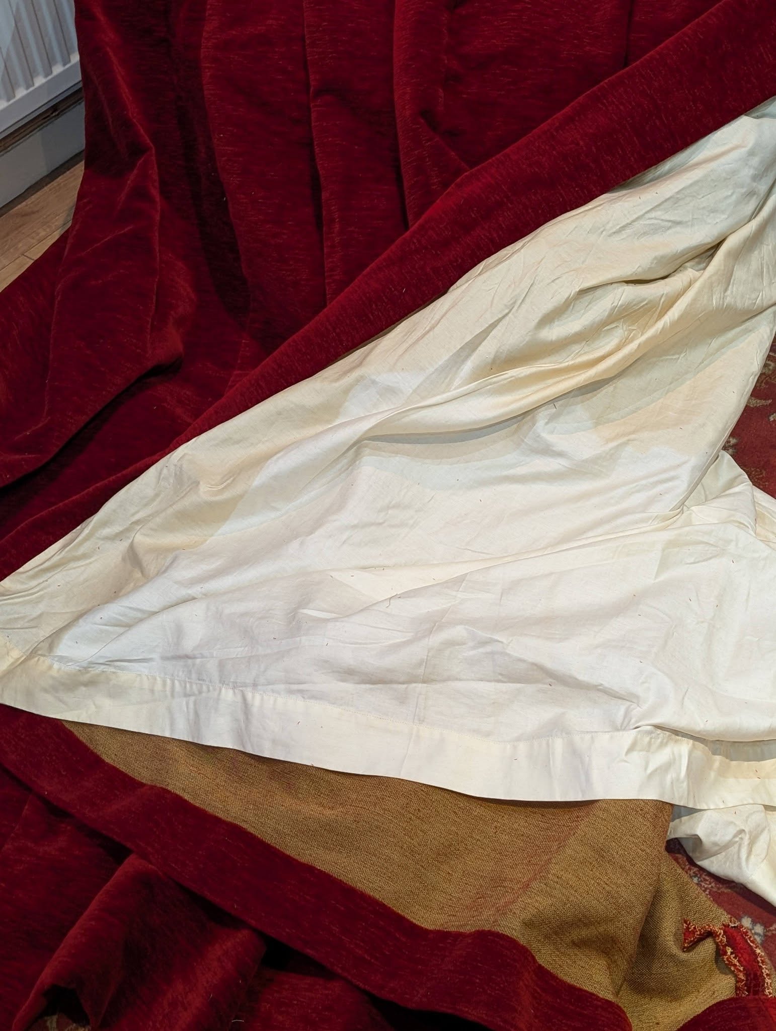 red5 - Divinely Vintage Interiors Close-up of overlapping burgundy velvet and cream fabric draped together on a wooden floor.