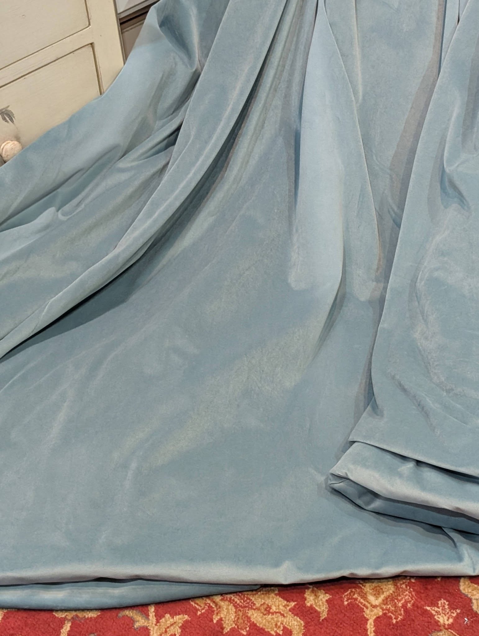 teal2 - Divinely Vintage Interiors Blue fabric draped over an unseen object, with a folded edge resting near a red patterned carpet.