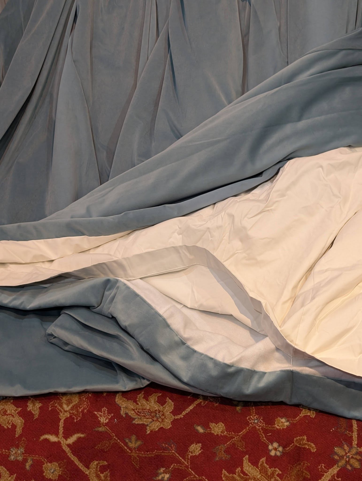teal5 - Divinely Vintage Interiors Blue and white bed sheets crumpled on a red patterned carpet, showing draped fabric and folds.