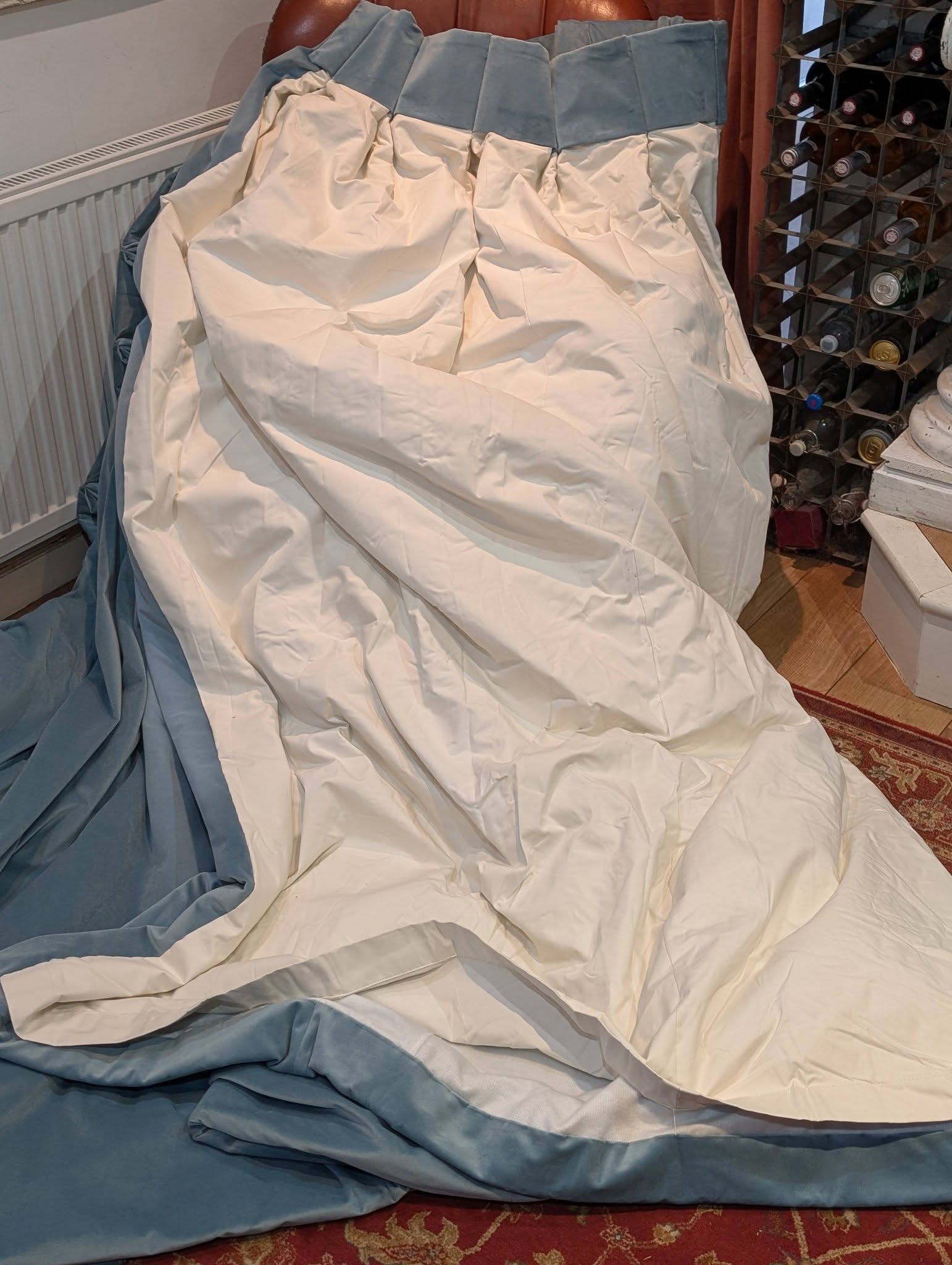 teal6 - Divinely Vintage Interiors Blue and white blanket crumpled on the floor next to a radiator and a wine rack in a corner room.