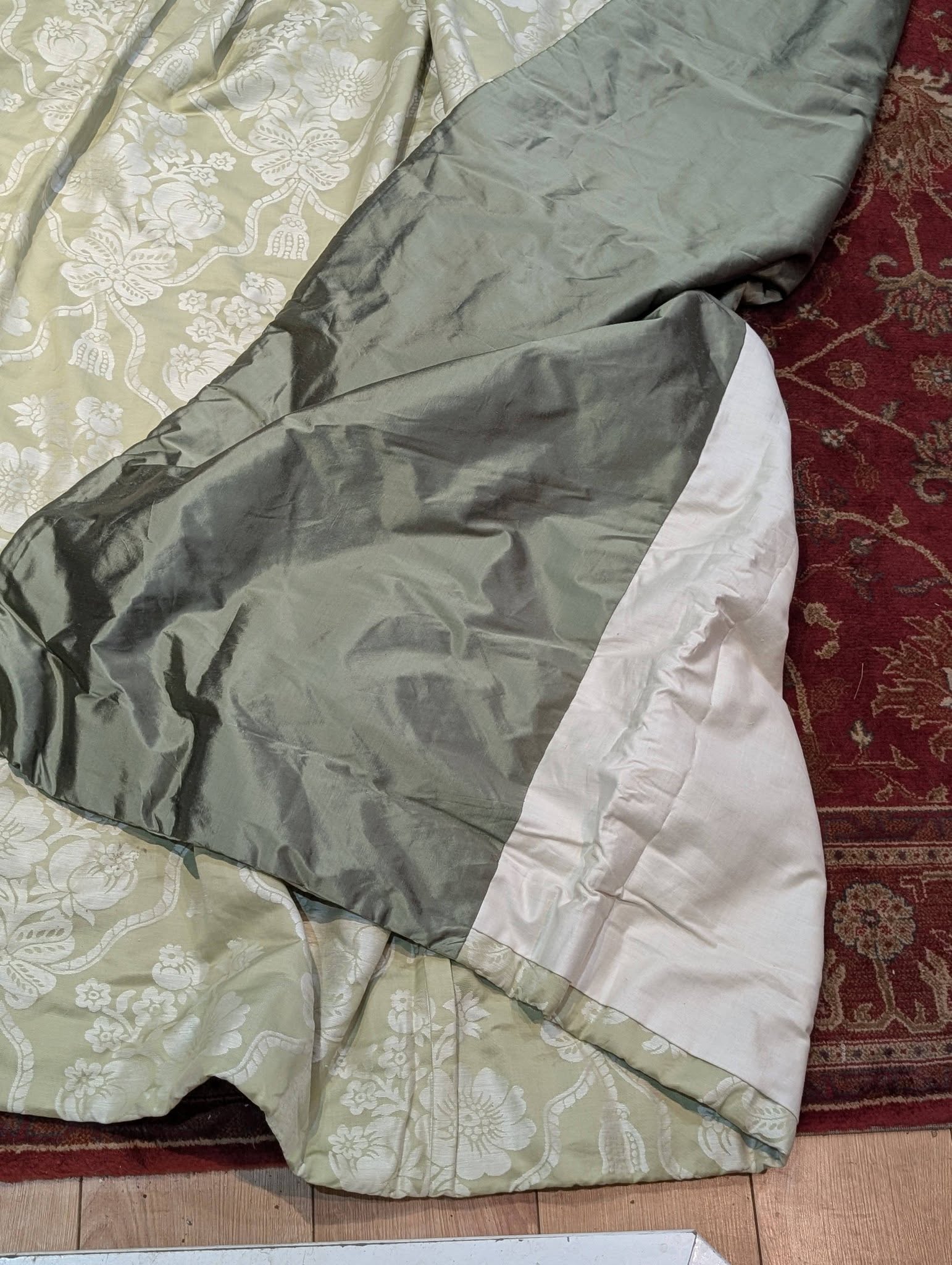 bed5 - Divinely Vintage Interiors Green floral comforter with a gray striped section draped over a bed on a red patterned rug.