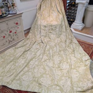 Pale green damask fabric draped over a standing form, creating a floor-length display in a vintage-styleVery Long Linen Damask Pinch Pleat Second-Hand Curtains – 2 Pairs Available.