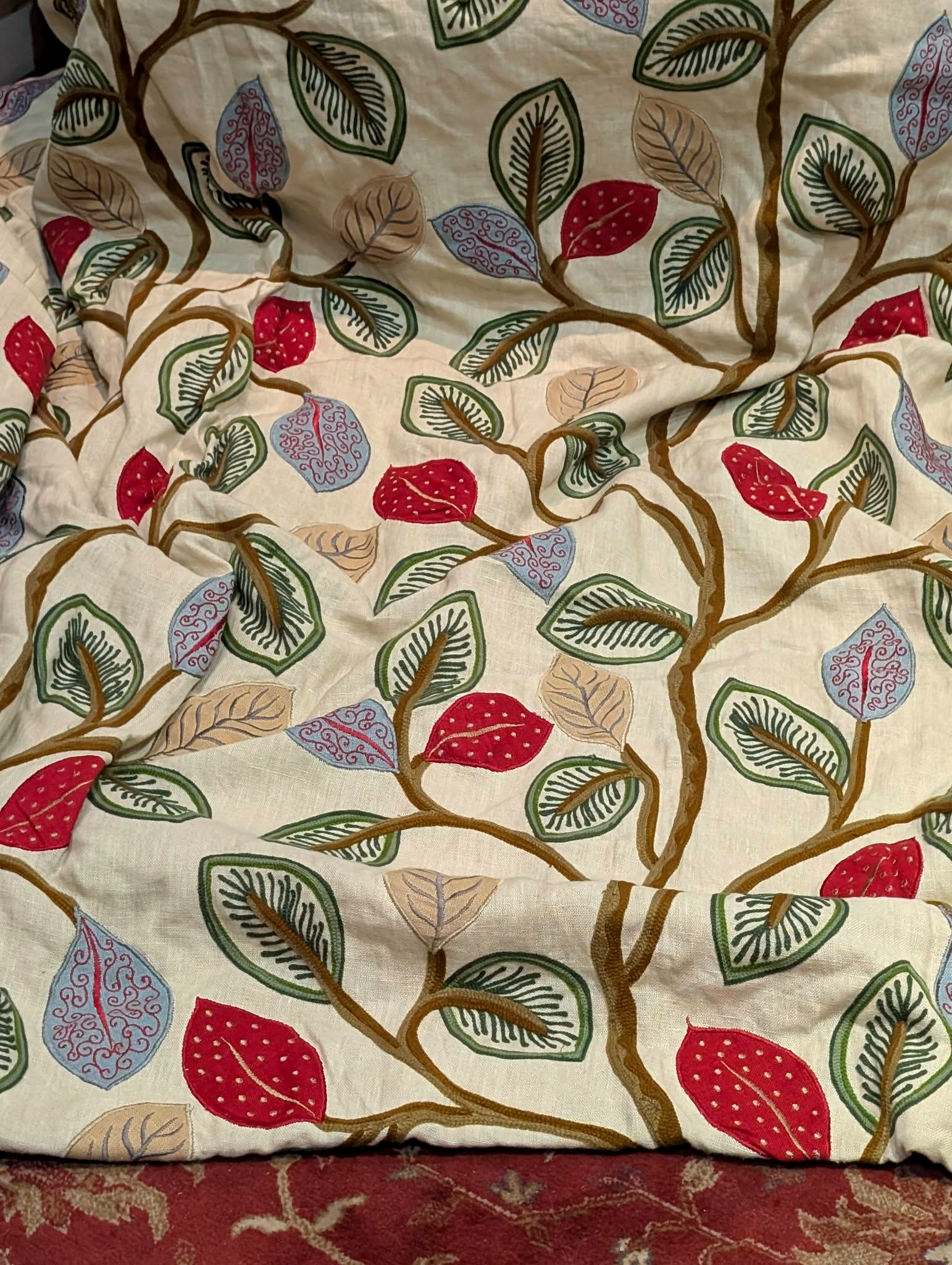 Close-up of cream fabric printed with brown twisting branches and multicolored leaves (red, blue, beige).