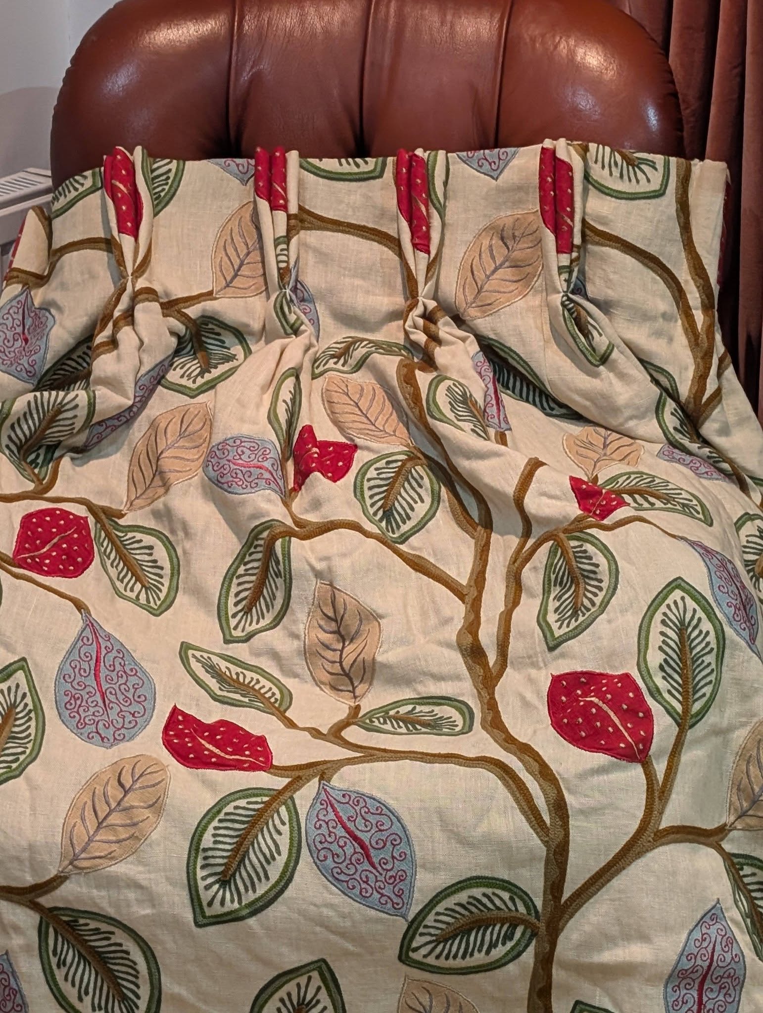 Beige bedspread with a brown tree branch pattern and multicolored leaves in red, green, and blue tones laid over a brown headboard-shaped background.