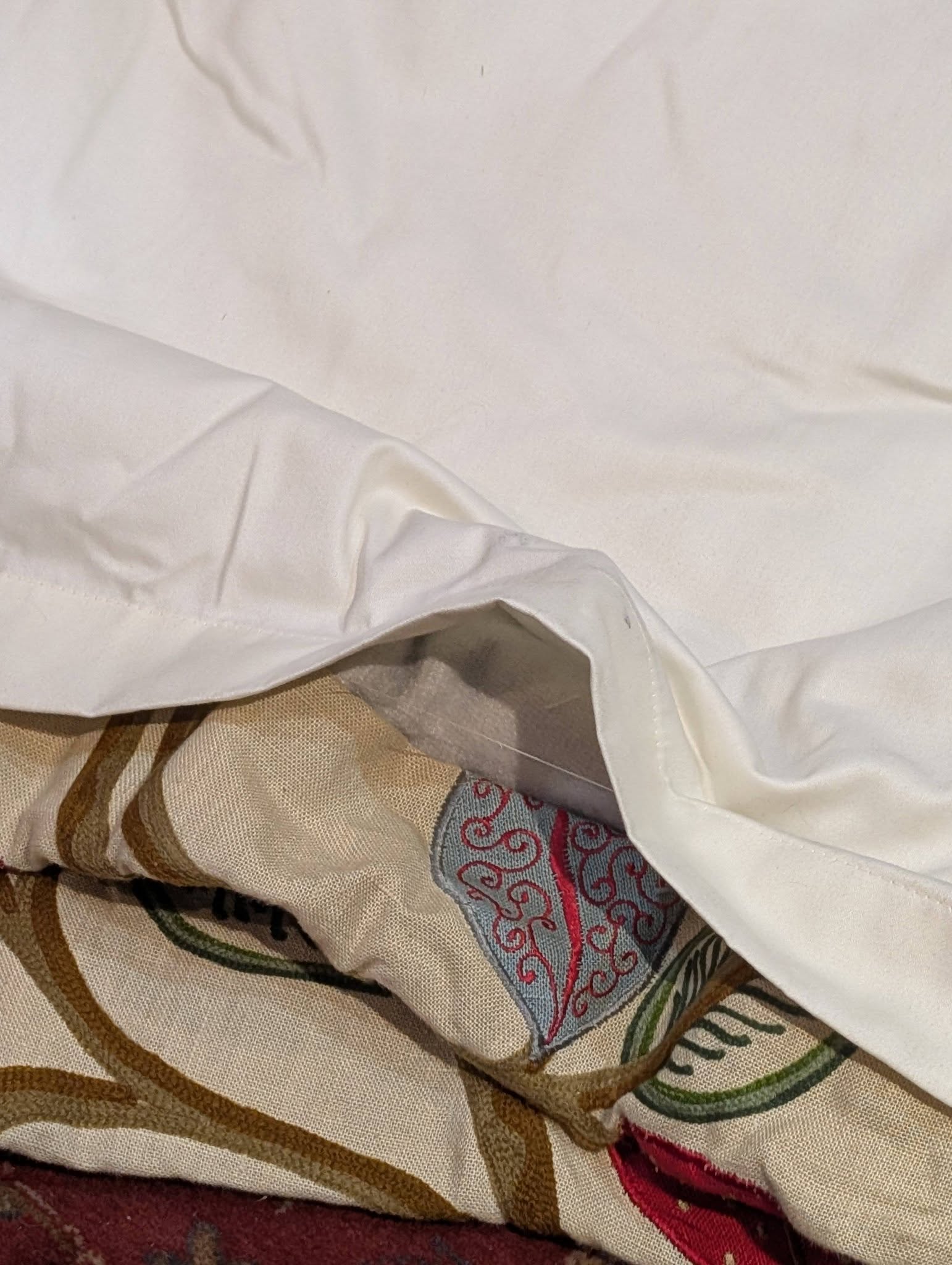 Close-up of layered fabrics: a white sheet over beige striped cloth with a red and gray patterned textile peeking out beneath.
