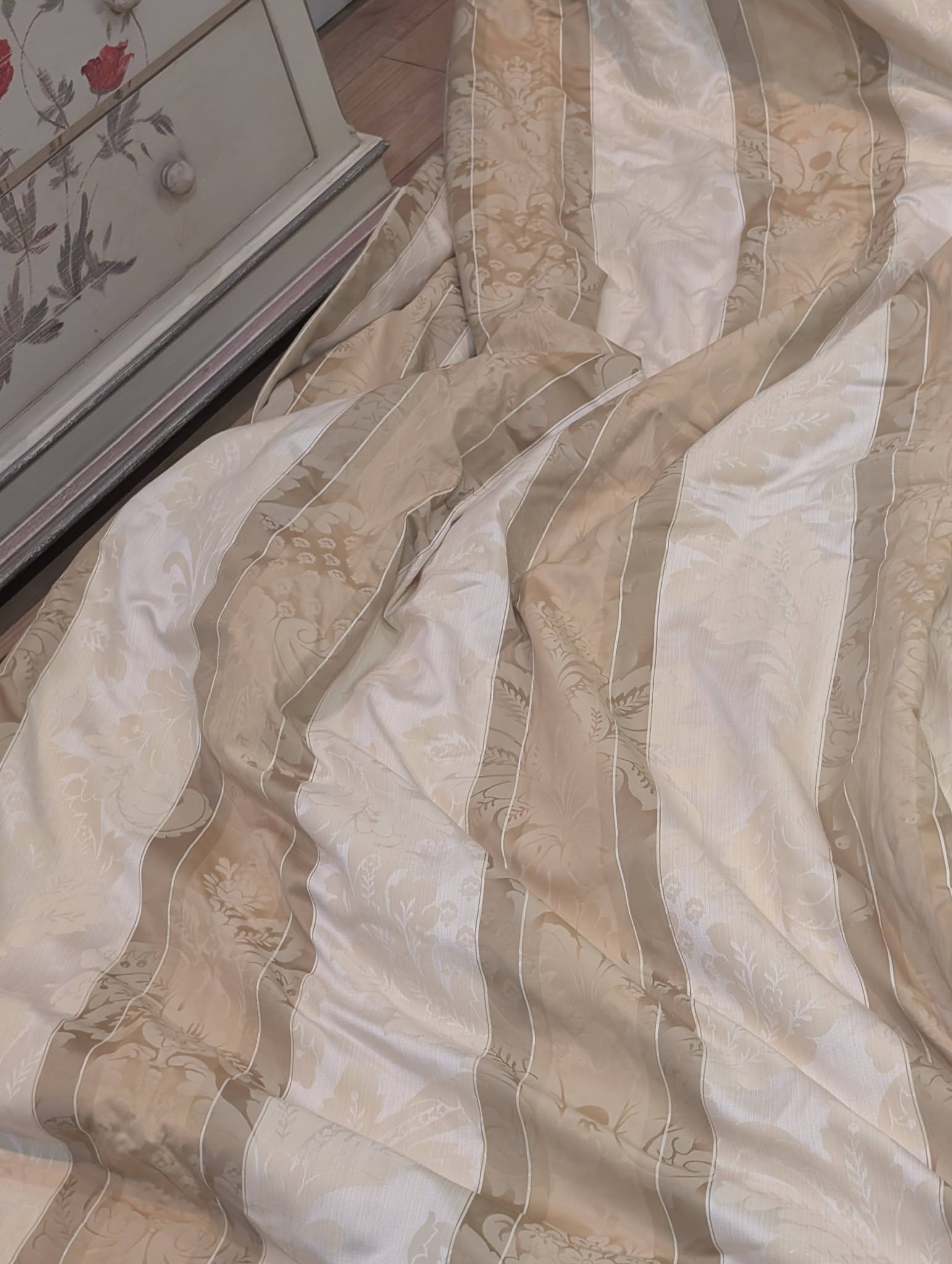 dam3 - Divinely Vintage Interiors Close-up of a beige floral-patterned comforter draped over a bed near a dresser edge.
