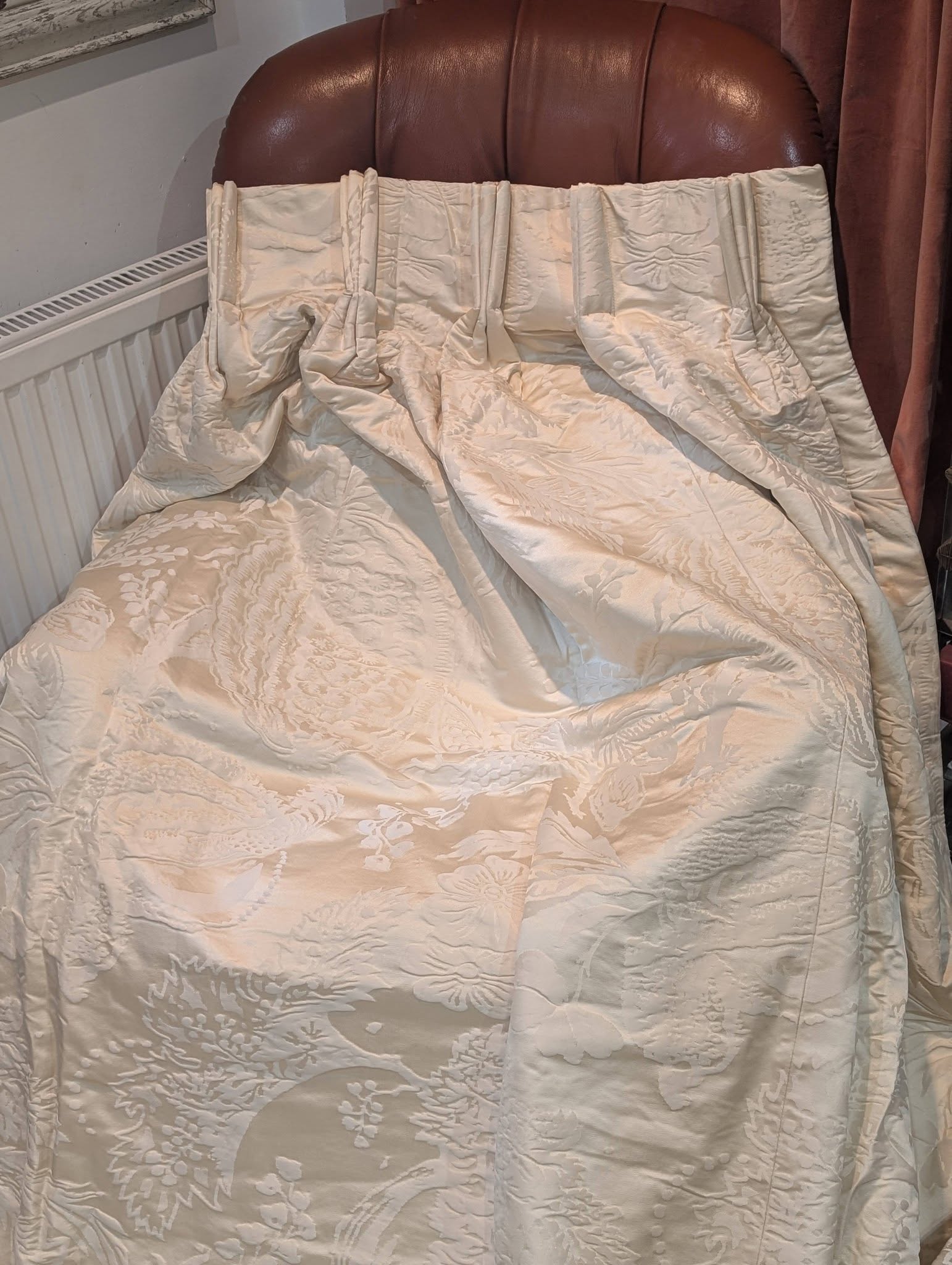 dam4 - Divinely Vintage Interiors Cream floral quilt laid over a bed with a brown leather headboard and burgundy curtains in the background.