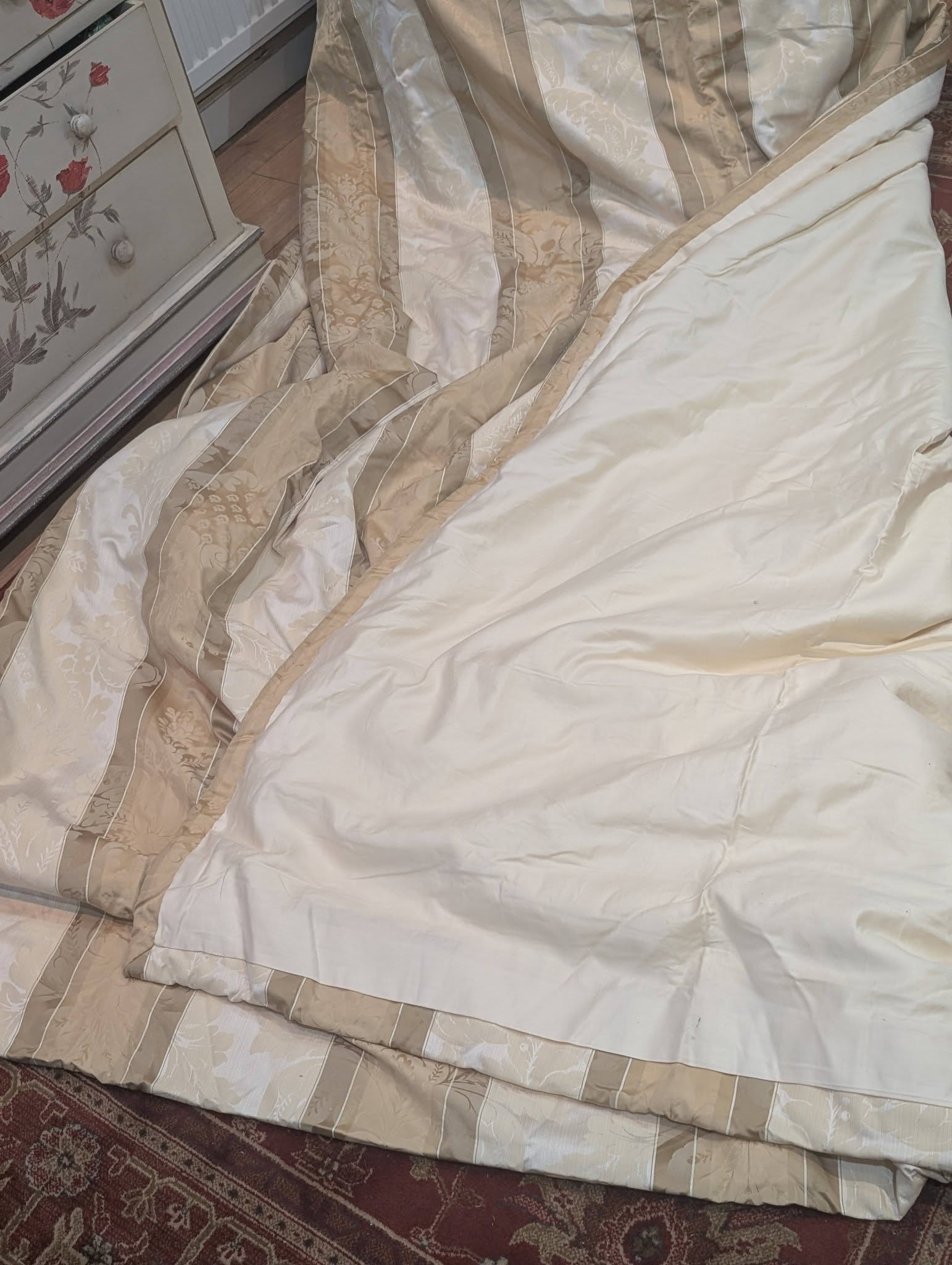 dam5 - Divinely Vintage Interiors Beige striped comforter laid over a mattress on the floor beside a floral dresser.