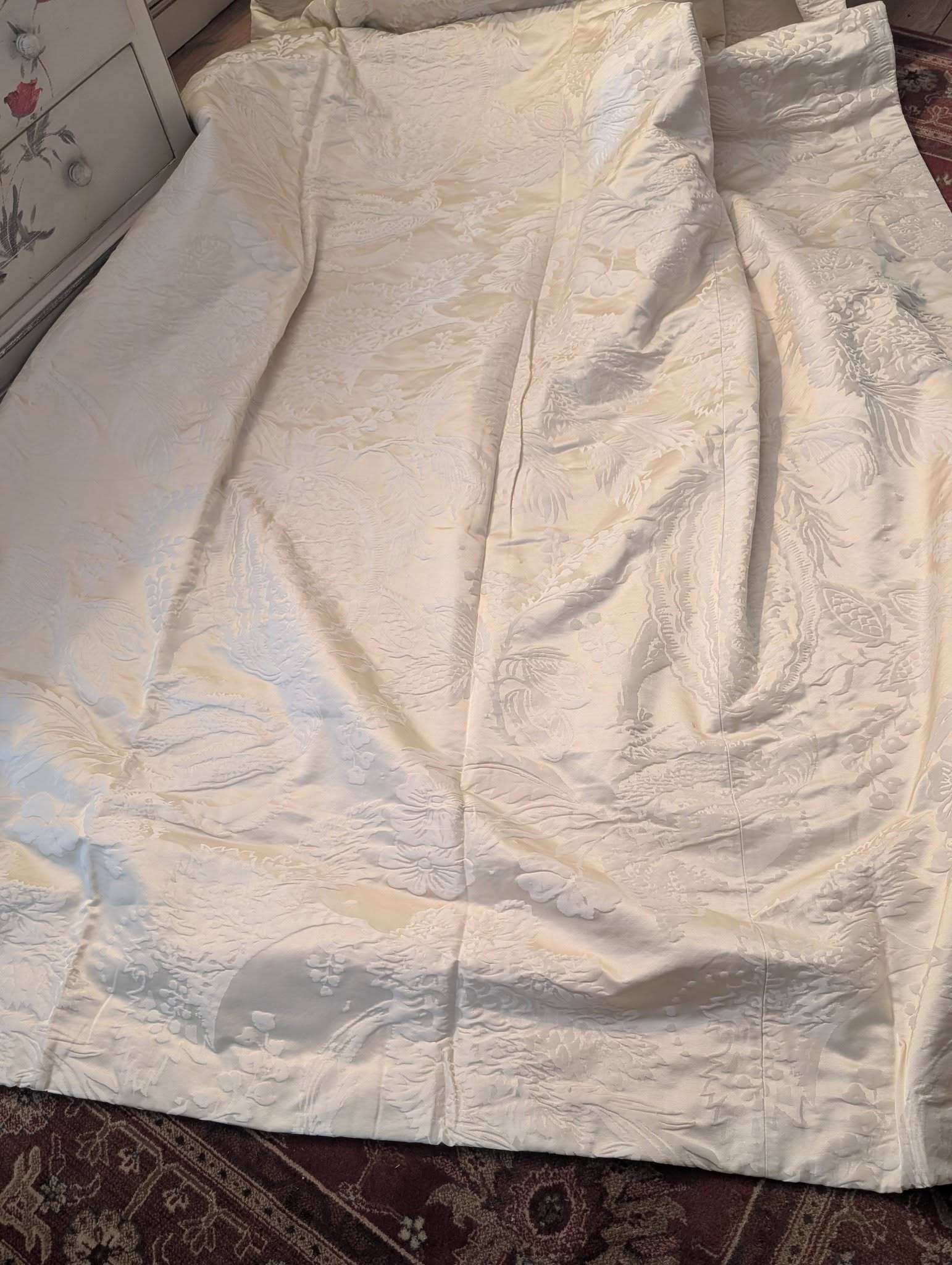 dam8 - Divinely Vintage Interiors White quilted comforter spread on a patterned rug, showing floral damask stitching and soft folds.