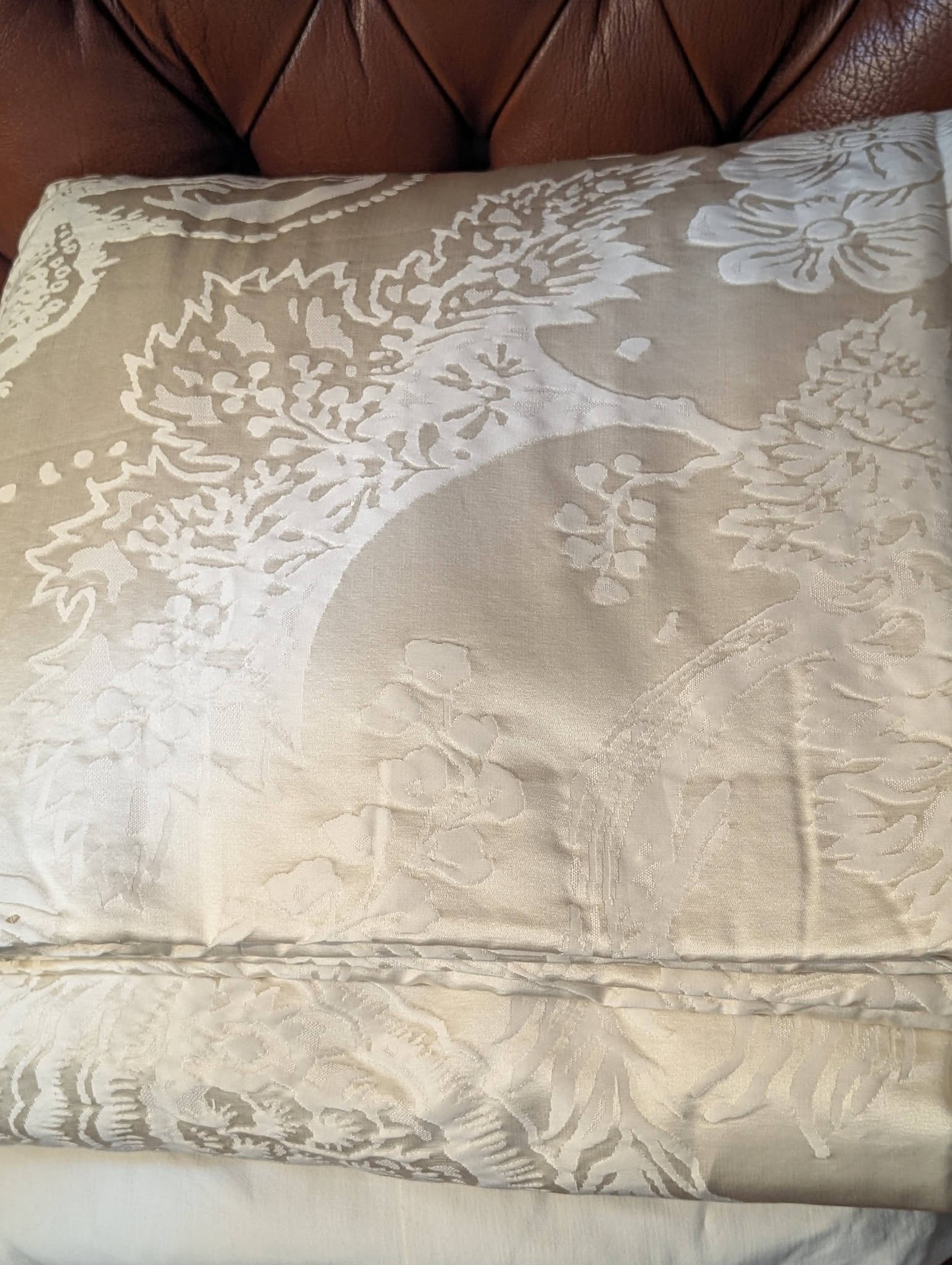 dma10 - Divinely Vintage Interiors Close-up of a beige floral quilted blanket draped over a brown leather couch, showing textured fabric patterns and stitching.
