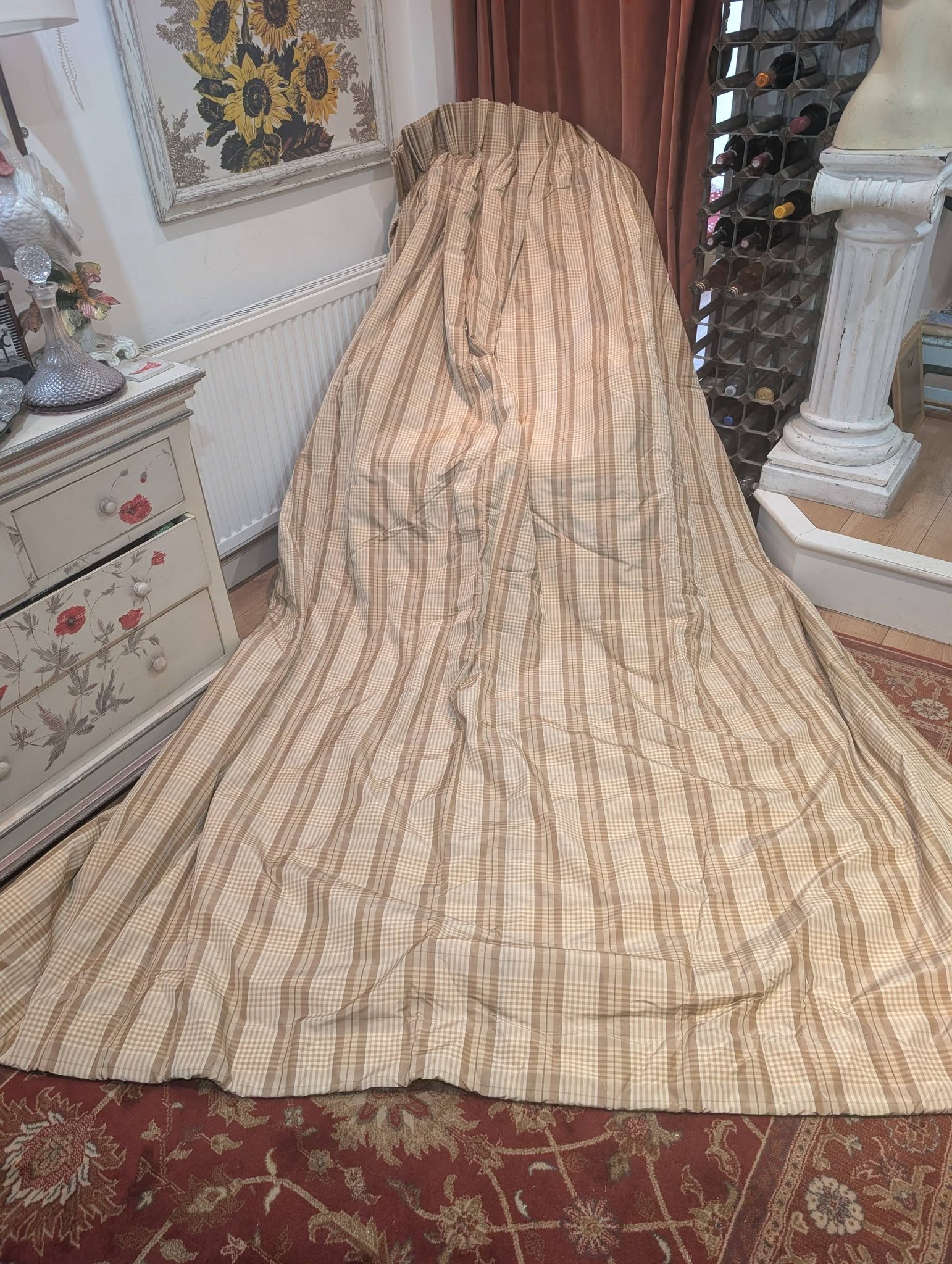 ging1 - Divinely Vintage Interiors Beige plaid fabric draped over furniture in a vintage-styled room with a sunflower painting and wine rack nearby.
