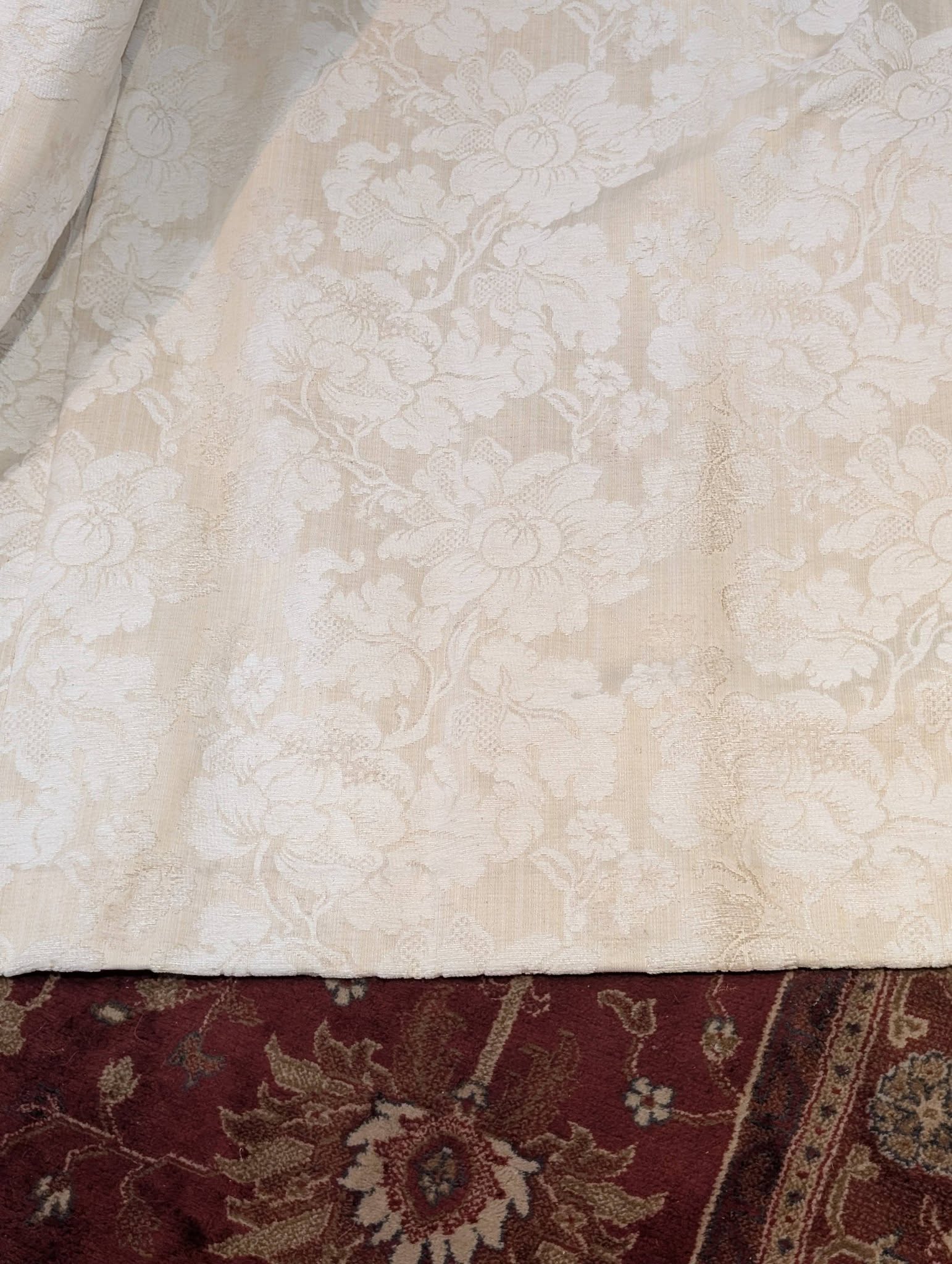 leila3 - Divinely Vintage Interiors Close-up of a light beige lace fabric draped over a dark patterned rug, showing texture.