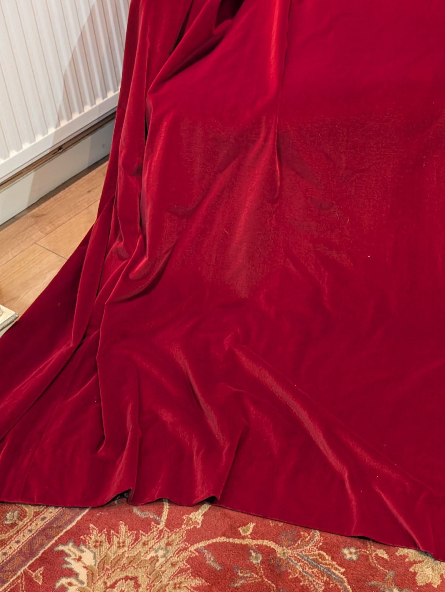 Red velvet fabric draped over furniture, pooling on a patterned rug with a white radiator in the background.