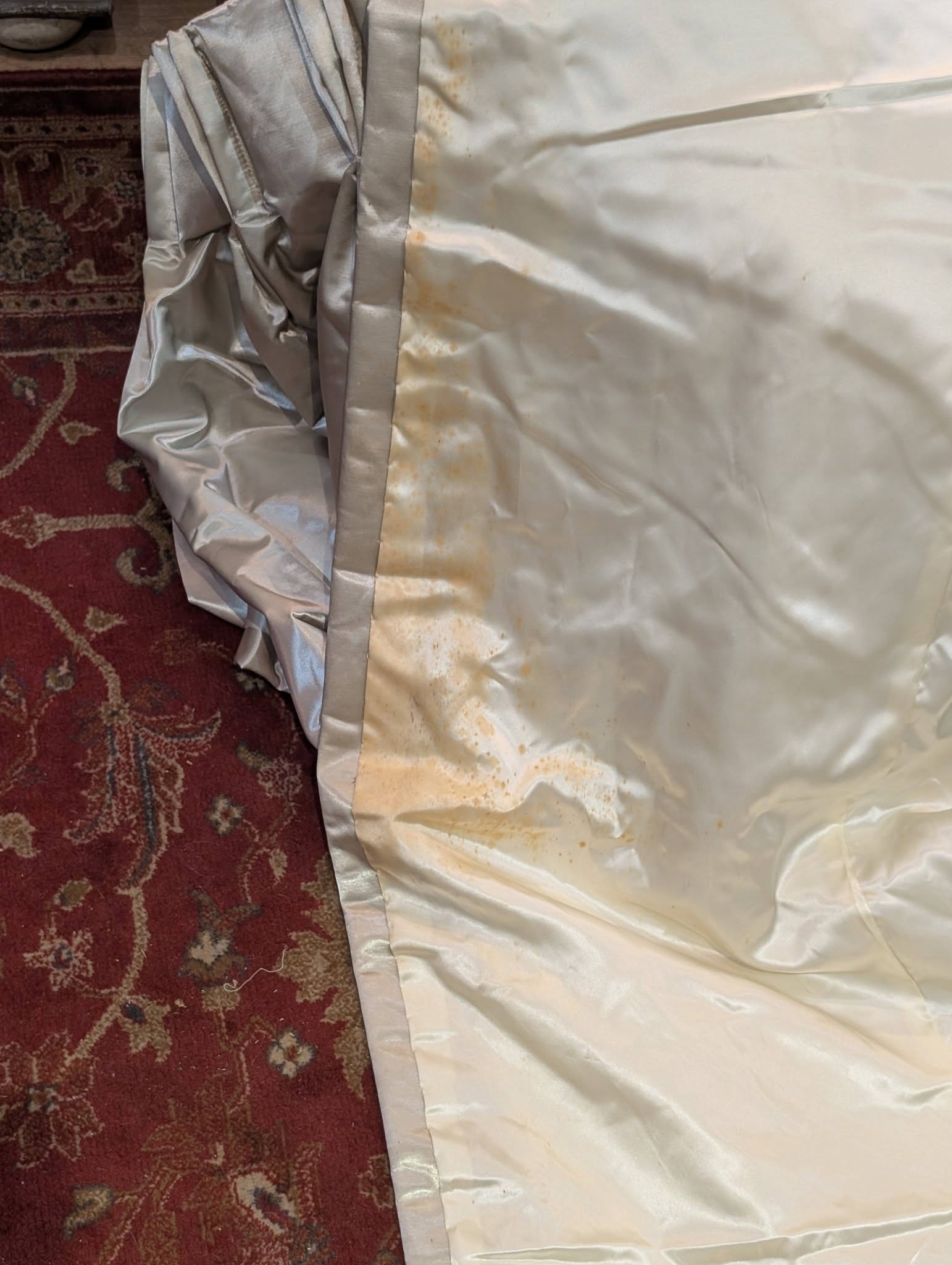 silk10 - Divinely Vintage Interiors Crinkled silver fabric or material spread over a red patterned rug with rust-colored stains along a seam.