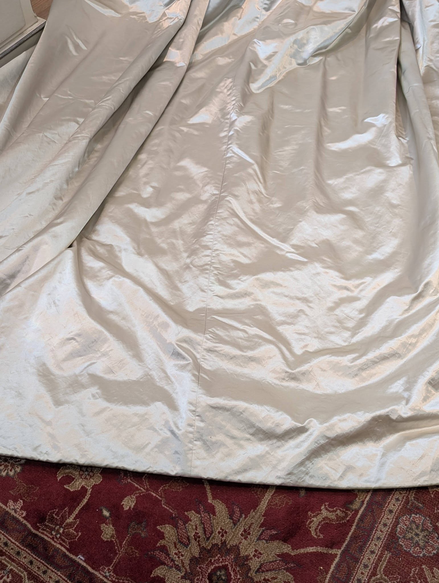 silk2 - Divinely Vintage Interiors Cream-colored fabric draped over an unknown object, resting on a red patterned rug with visible folds and creases.