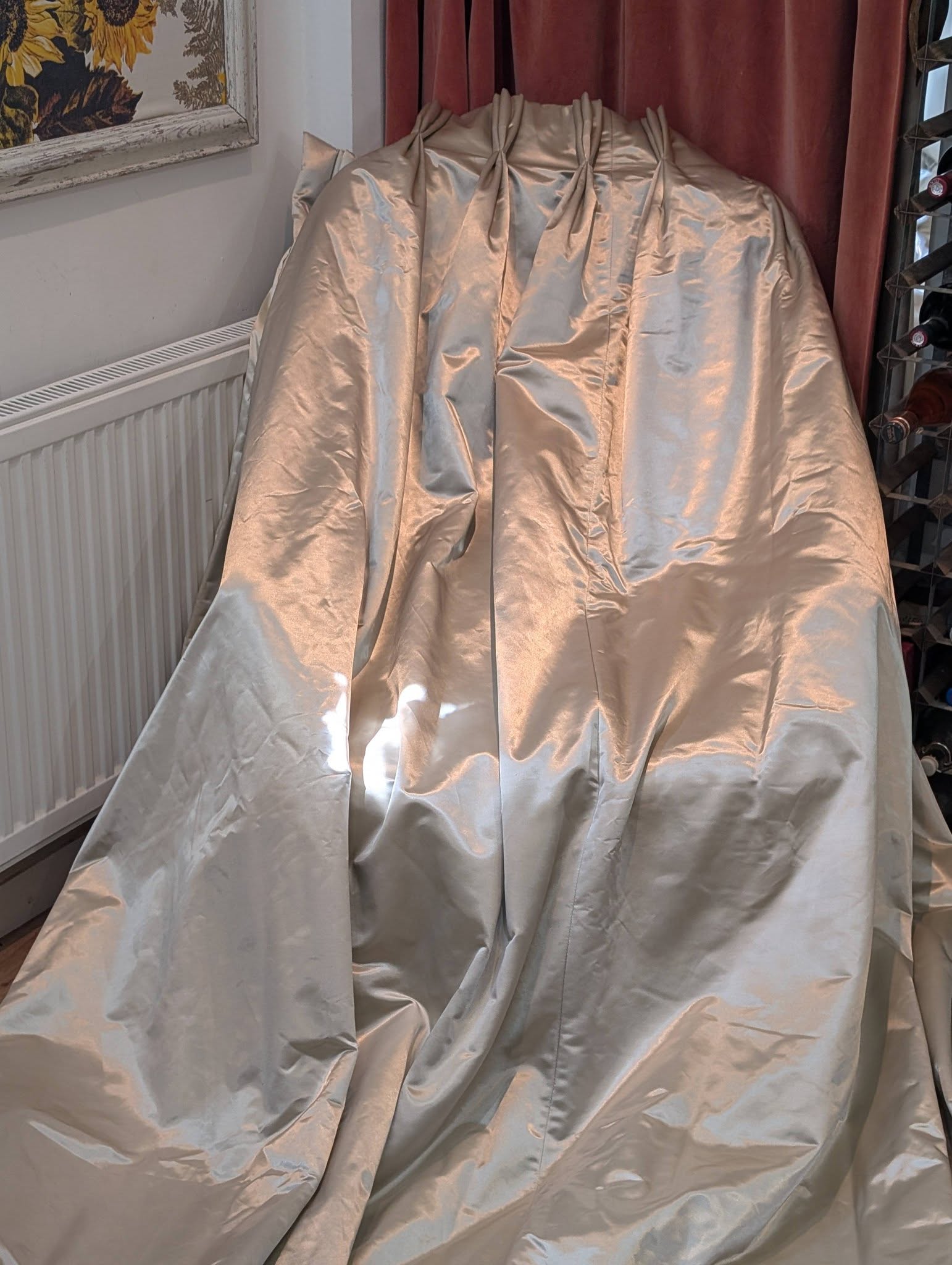 silk3 - Divinely Vintage Interiors Shiny silver satin garment draped over an object, covering its shape in a corner near a radiator and a wine rack.