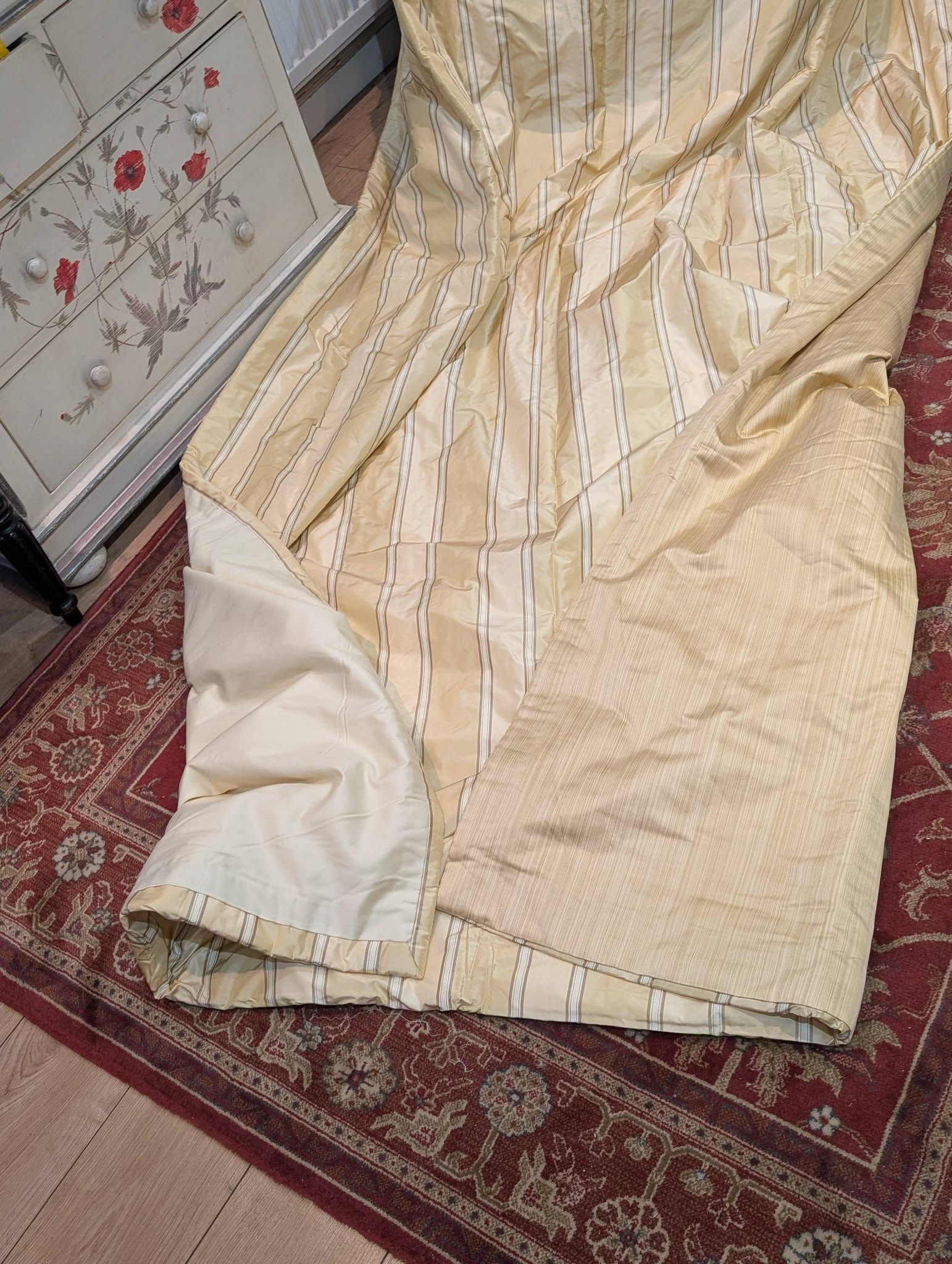 silk4 - Divinely Vintage Interiors Cream-striped bedding (duvet) spread over a red patterned rug beside a floral white dresser like a display setup.