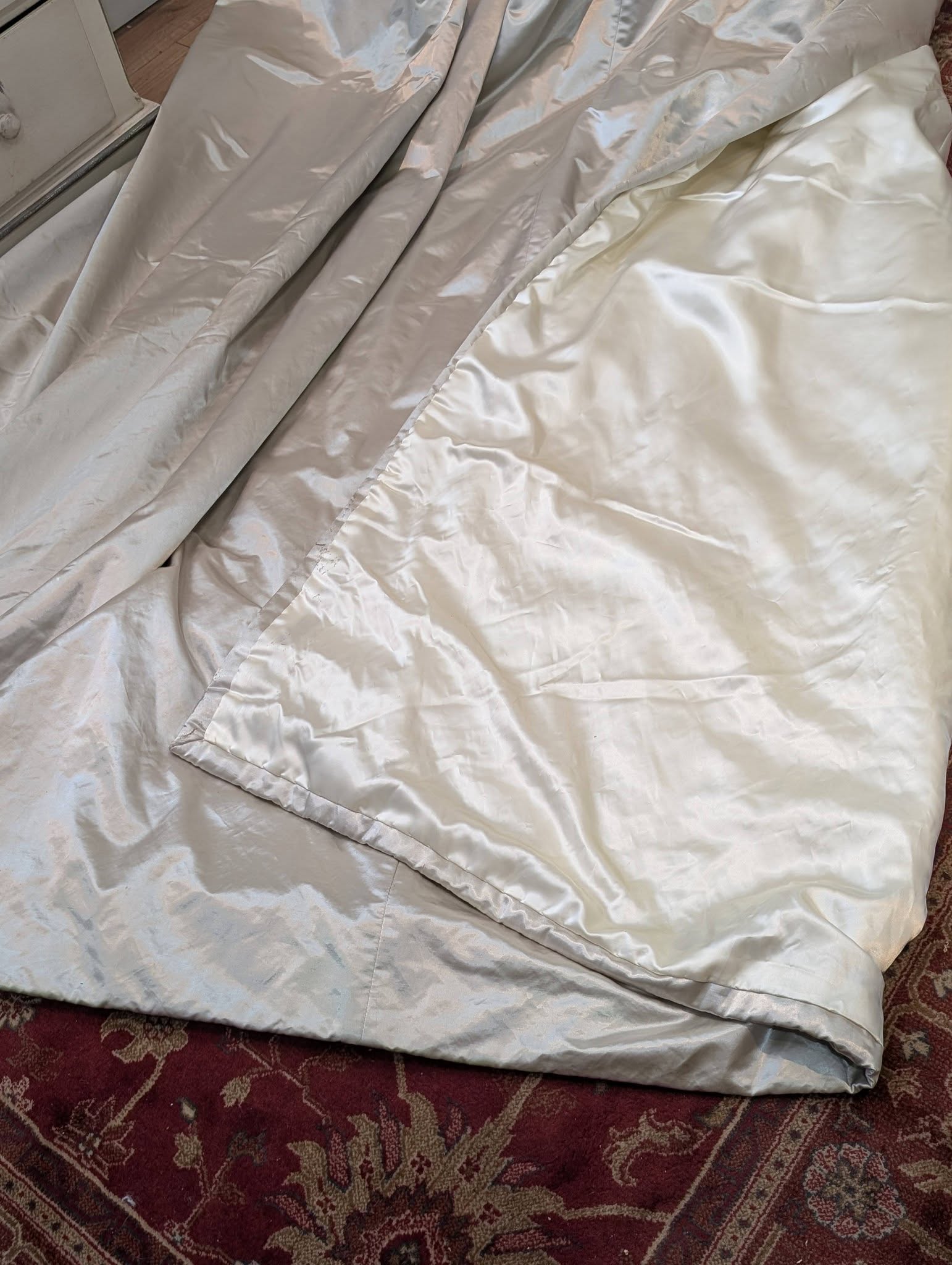 silk4 - Divinely Vintage Interiors Light gray satin comforter and sheets crumpled on a burgundy patterned rug floor.