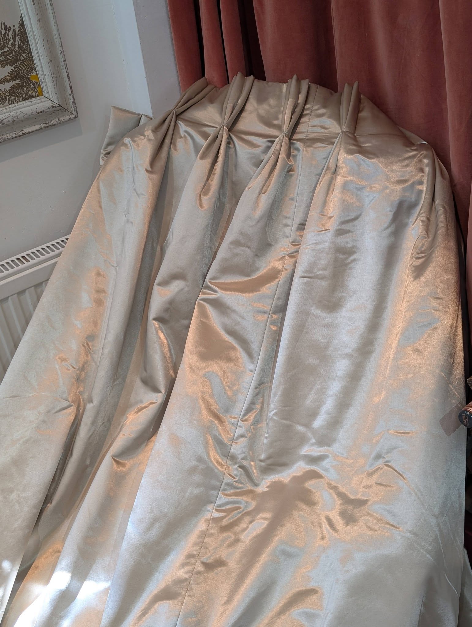 silk5 - Divinely Vintage Interiors Satin silver curtains tied in pleats hanging beside a burgundy curtain in a sunlit room corner.