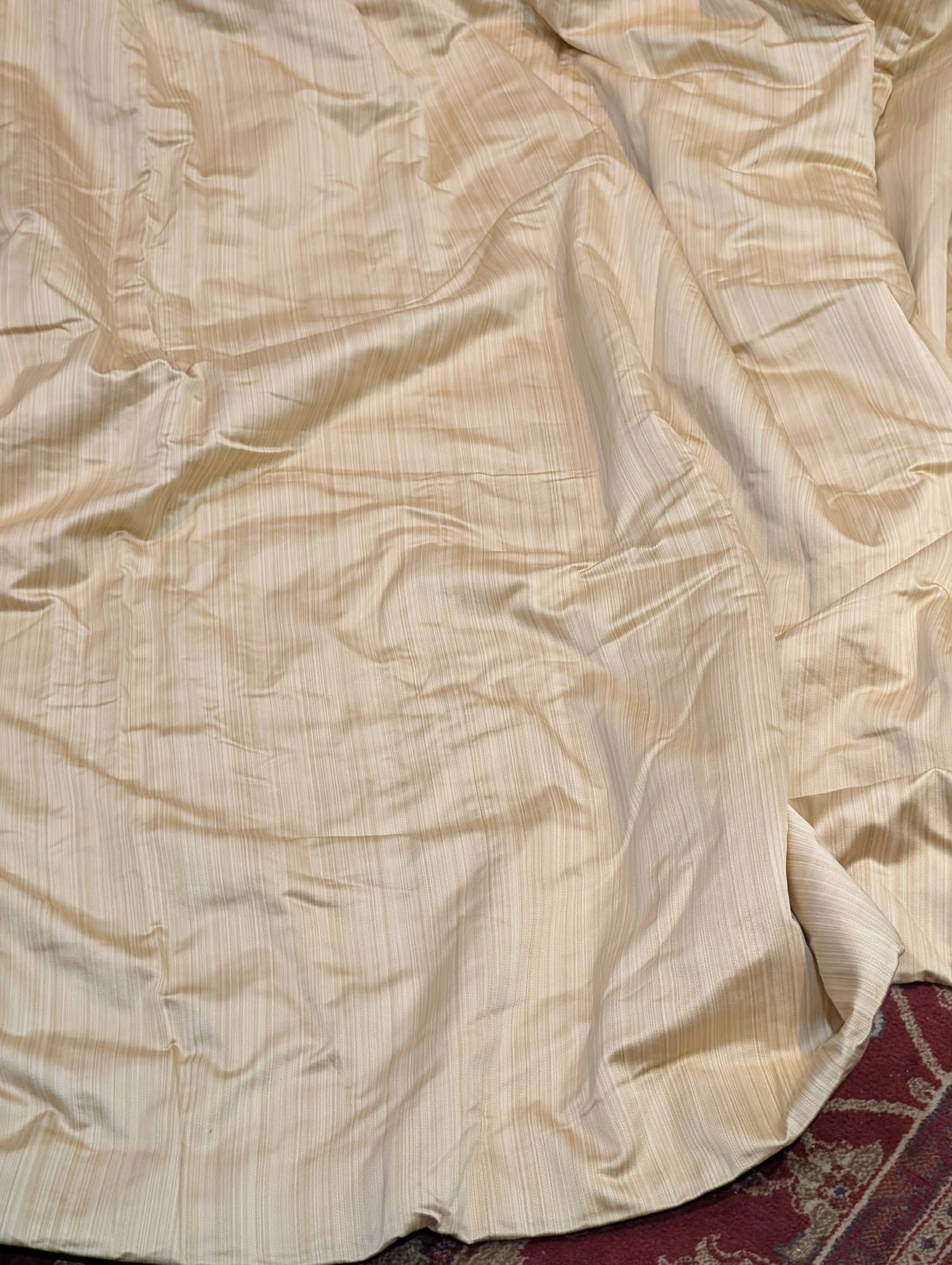 single2 - Divinely Vintage Interiors Beige striped bedsheet crumpled across a surface, with a red patterned carpet edge visible.