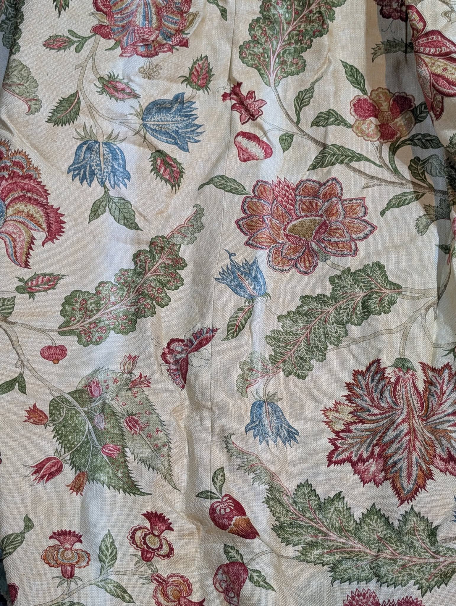Decorative floral fabric pattern with large red, pink, and blue flowers and green leaves on a beige background.