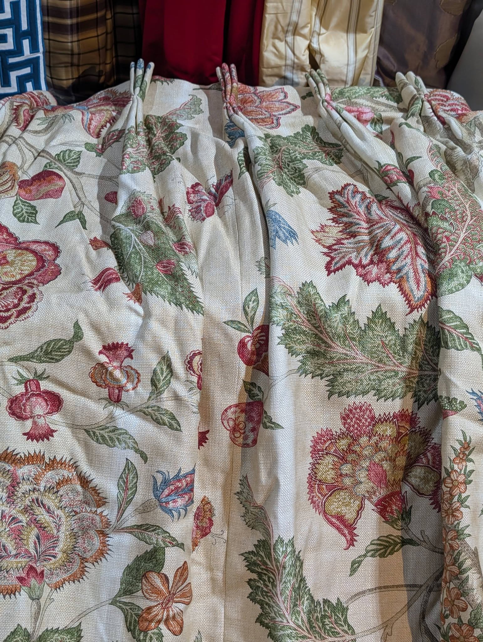 Close-up of a cream fabric with a bright floral botanical print and stitched pleats, with assorted pillows in the background.